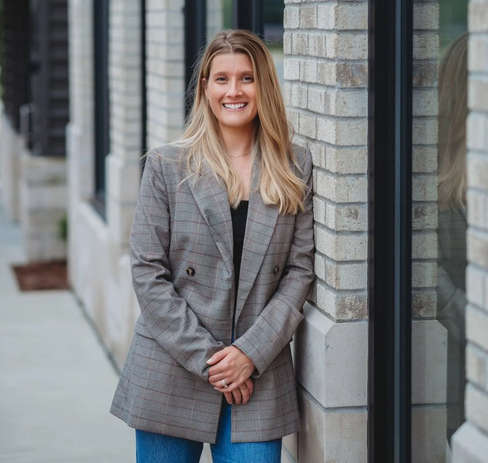 Carley Rollins, licensed nutritionist and board-certified health coach, smiling beside a brick wall in a plaid blazer.