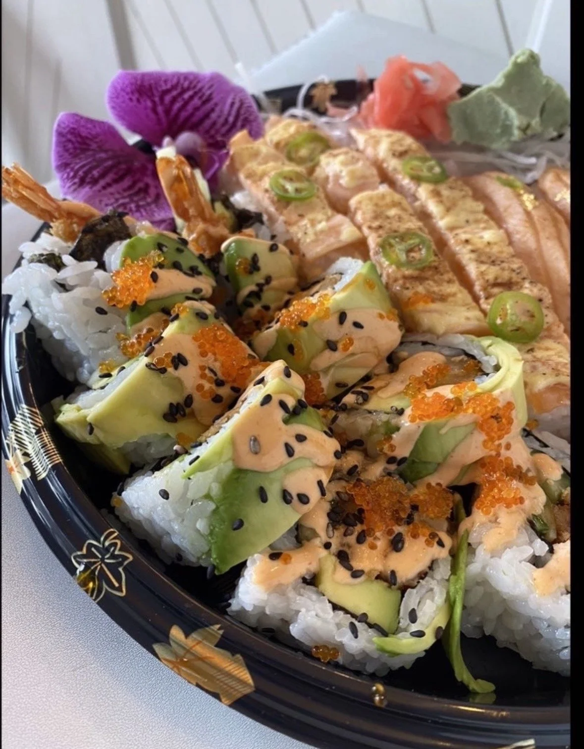 Assorted sushi platter with avocado rolls, spicy mayo, tobiko, black sesame seeds, shrimp, salmon, jalapeños, and orchids