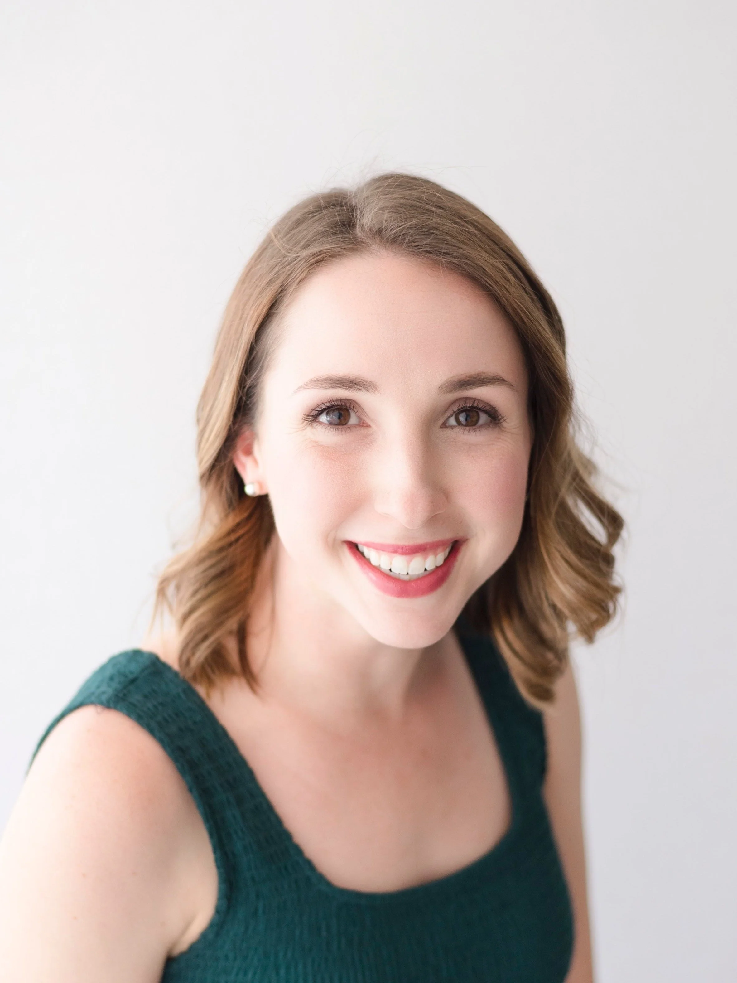 Smiling young woman with shoulder-length brown hair, wearing a sleeveless teal top, against a plain white background.