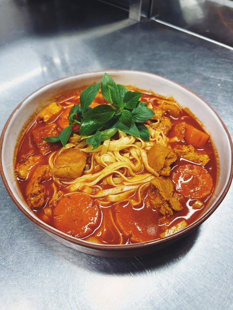 Bowl of noodle soup with meat, vegetables, and fresh basil garnish