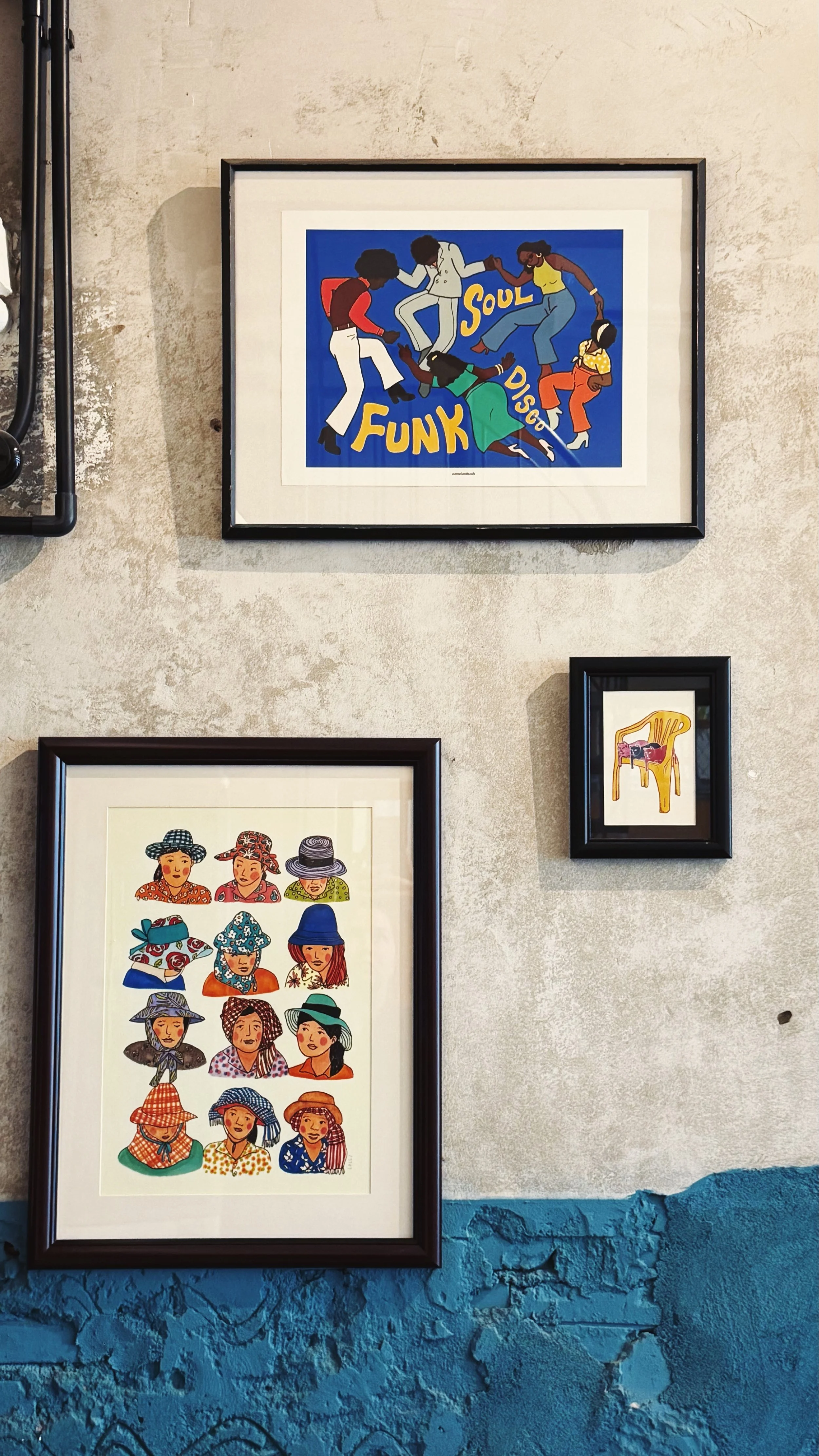 Various framed artworks on a textured wall, including a colorful illustration of people dancing with the words "FUNK SOUL DISCO," a portrait of women in hats, and a small illustration of a yellow chair with a cat on it.
