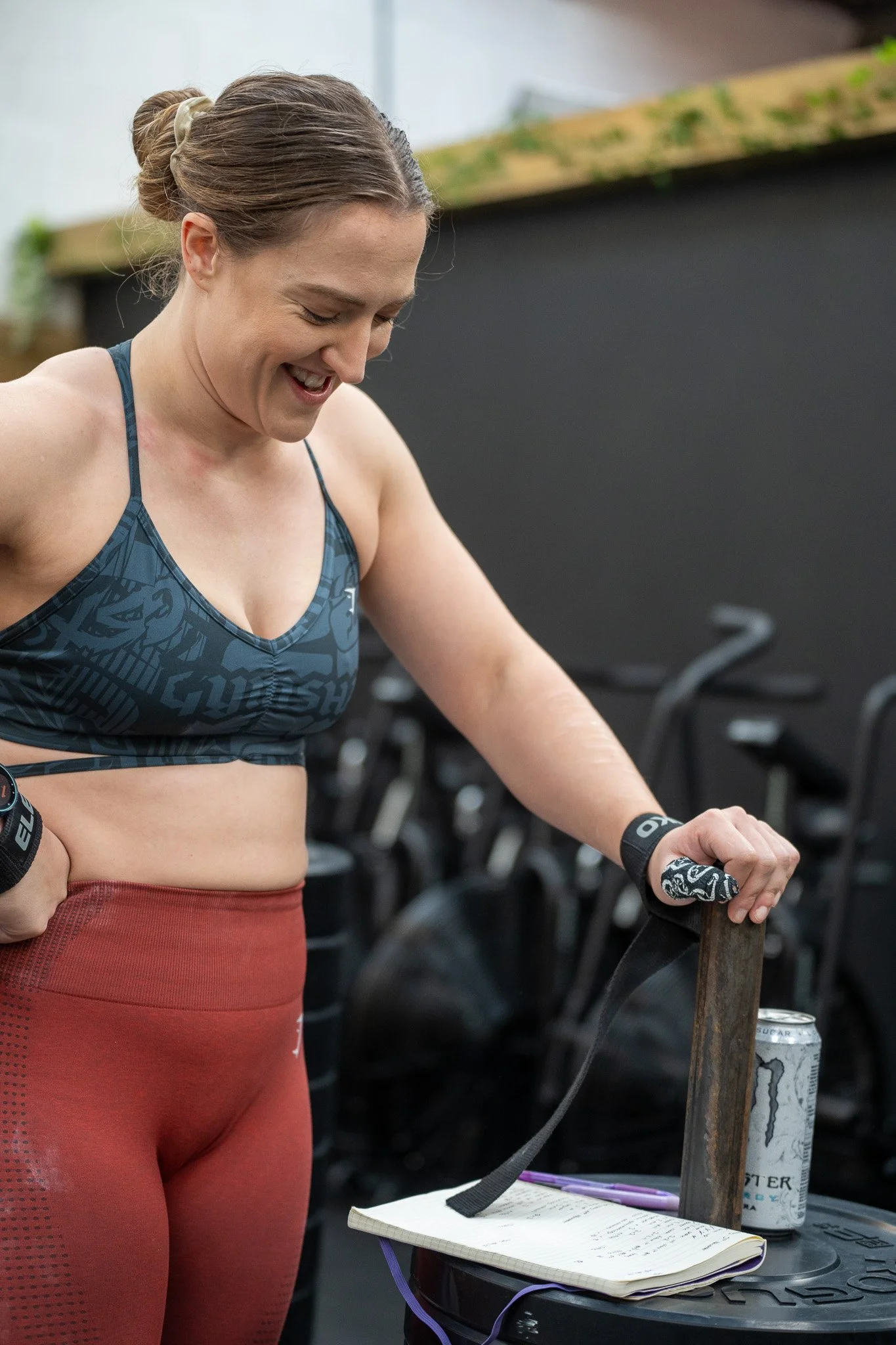 an athletic woman in a blue sports bra and red leggings smiling at her training diary