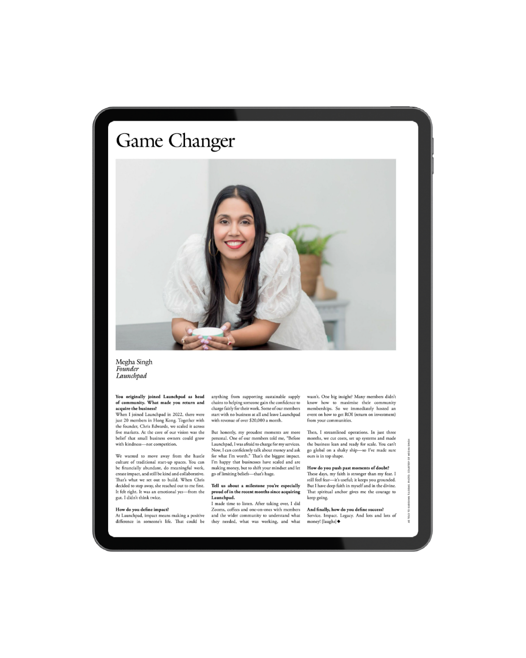 A digital tablet displaying a magazine article titled 'Game Changer' featuring a woman with long dark hair, wearing a white blouse, smiling and holding a coffee mug in a modern, bright room with a plant in the background.