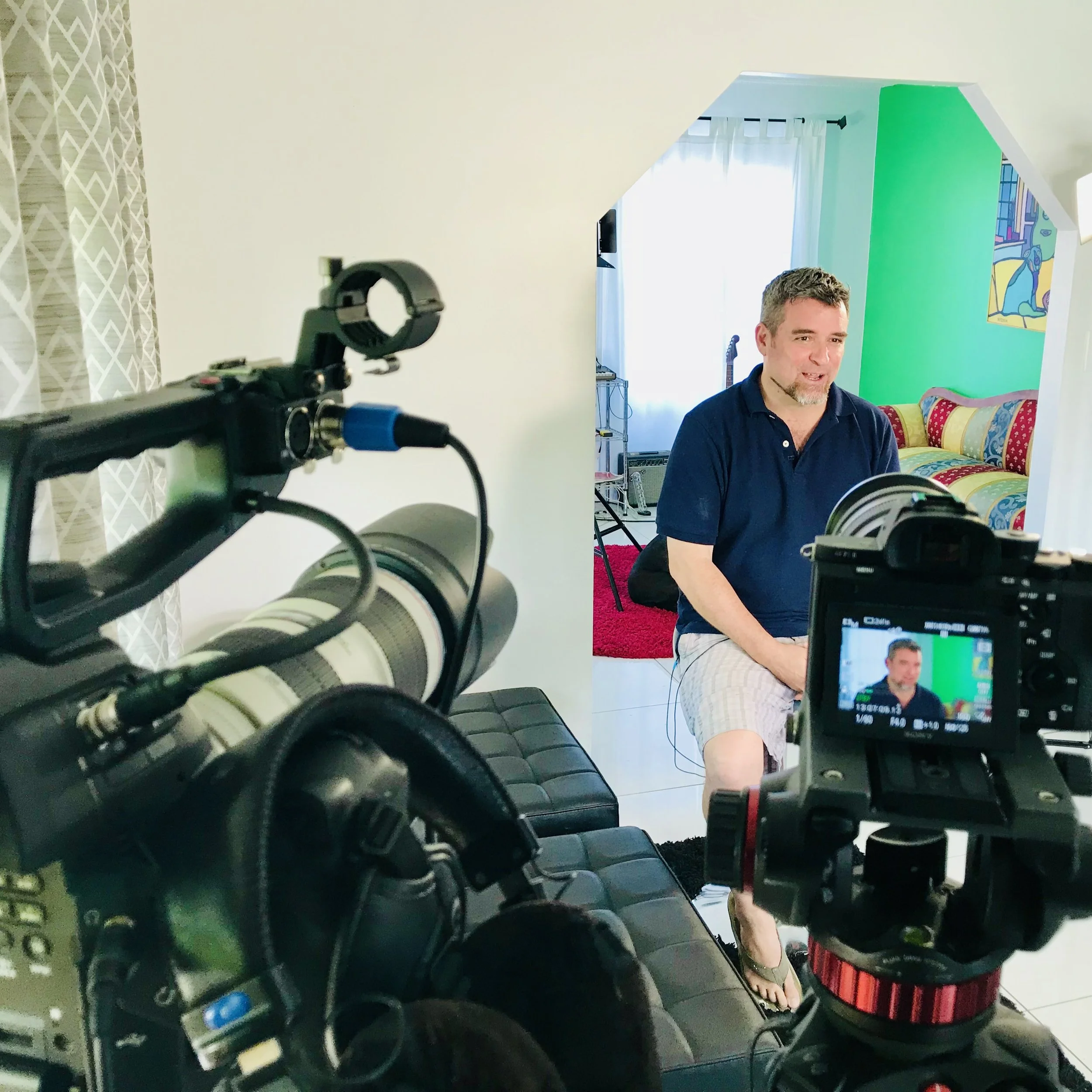 Key West author David L. Sloan sitting in front of a camera during a video shoot in a colorful, well-lit room.