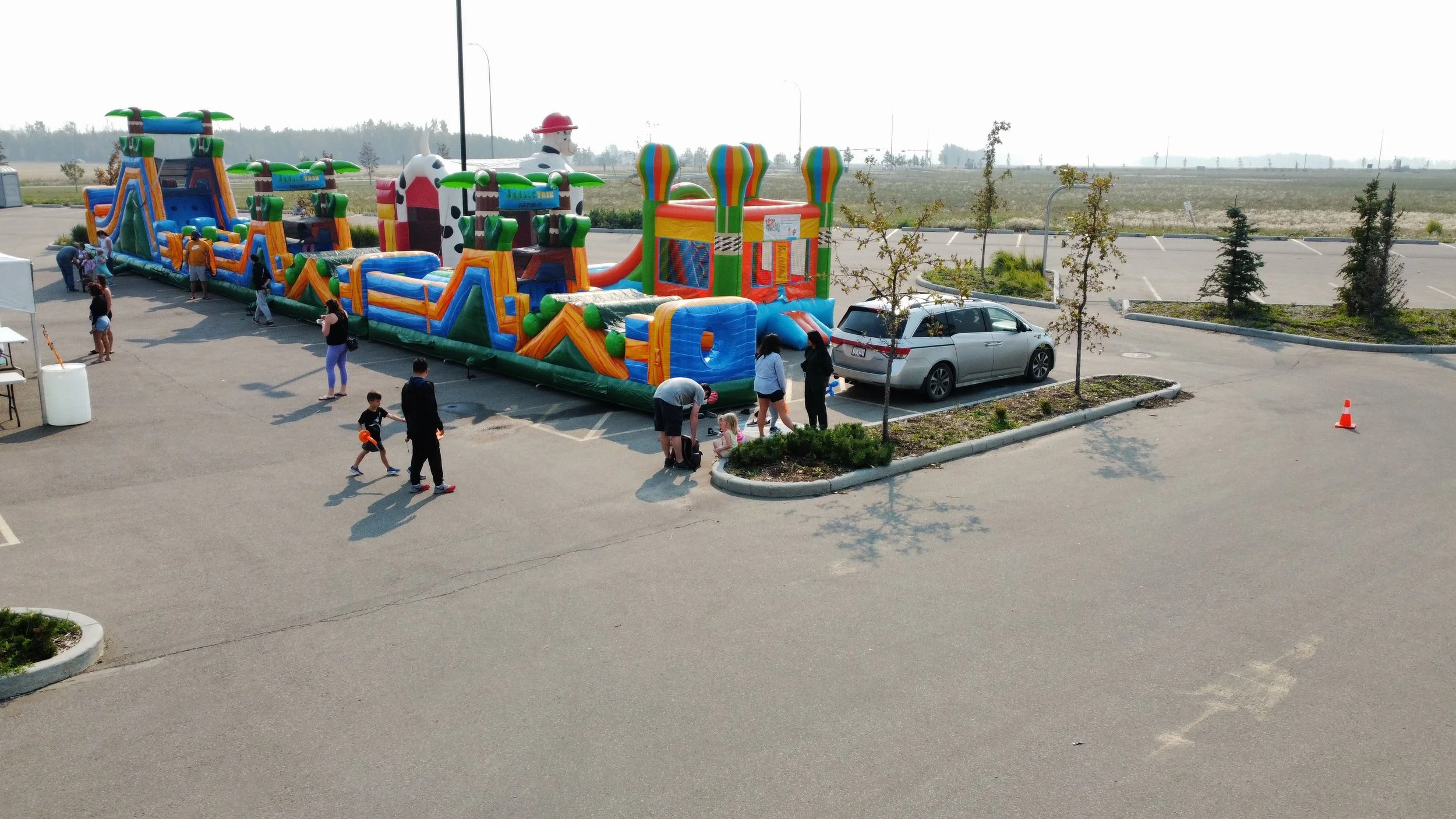 Colorful inflatable bounce houses in an outdoor parking lot with children and adults nearby, some preparing to enter or watch the bounce houses.