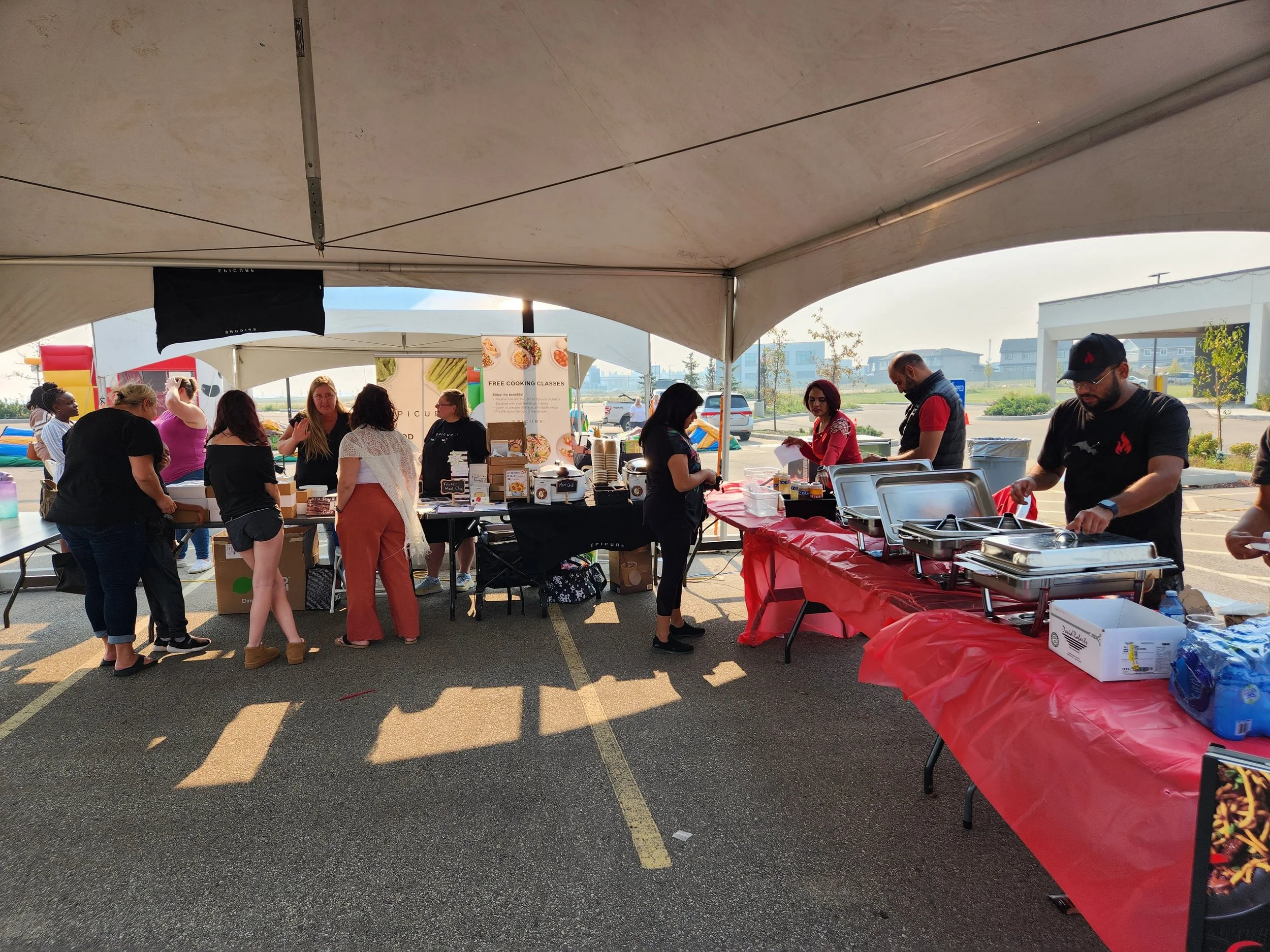 People lining up at food tents during an outdoor event, with volunteers serving food at a buffet table under a large tent.