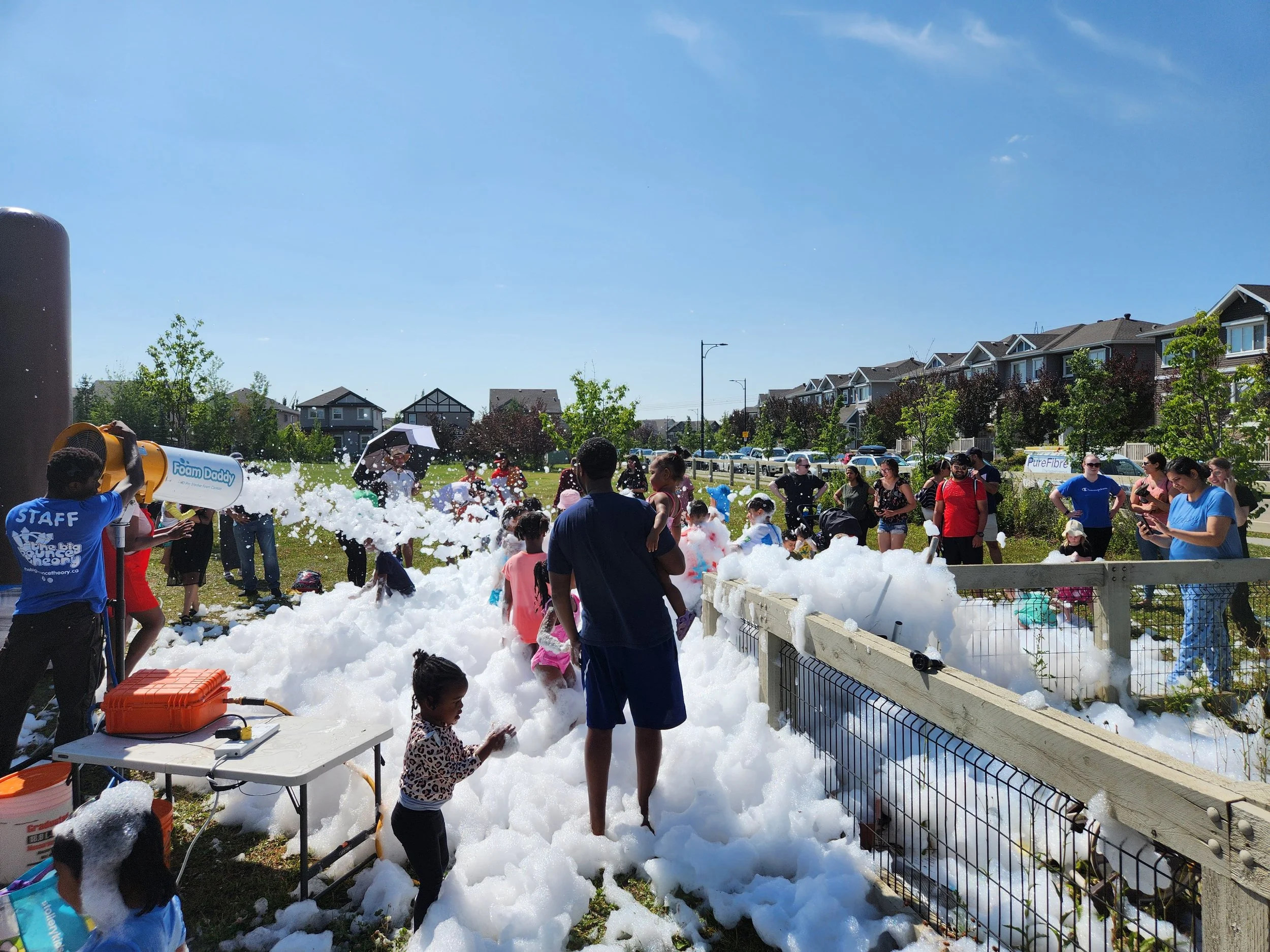 People at an outdoor foam party enjoying foam and bubbles on a sunny day in a residential area.