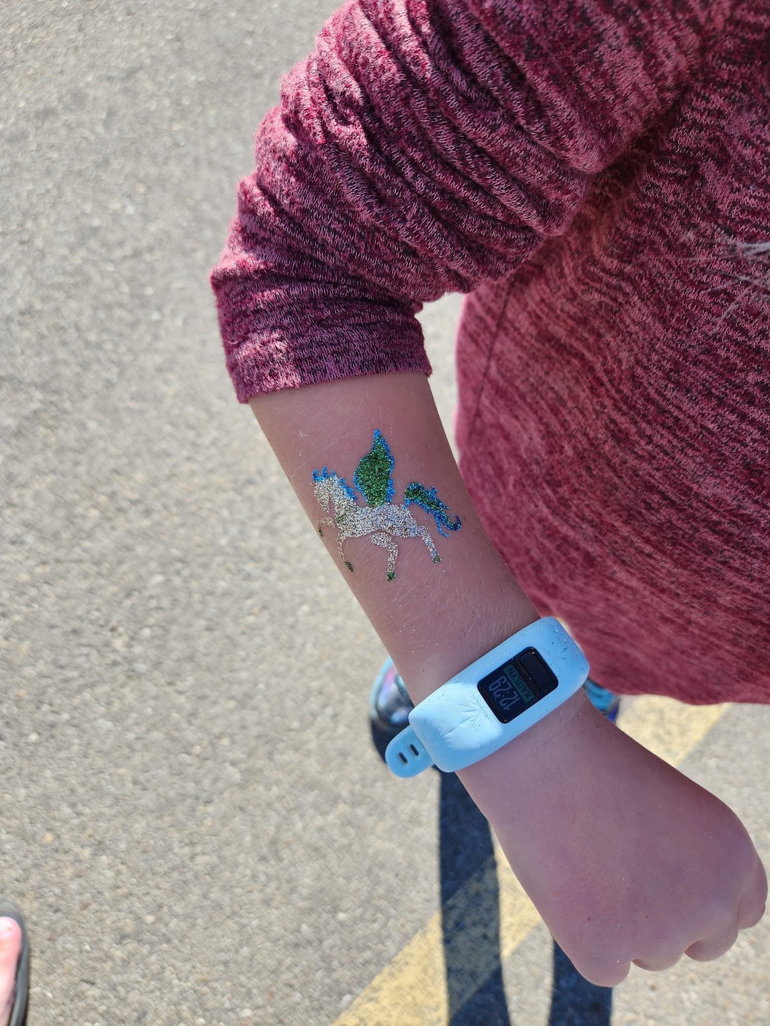 Person shows arm with a glittery unicorn tattoo, wearing a white fitness band, and dressed in a long sleeve red shirt.