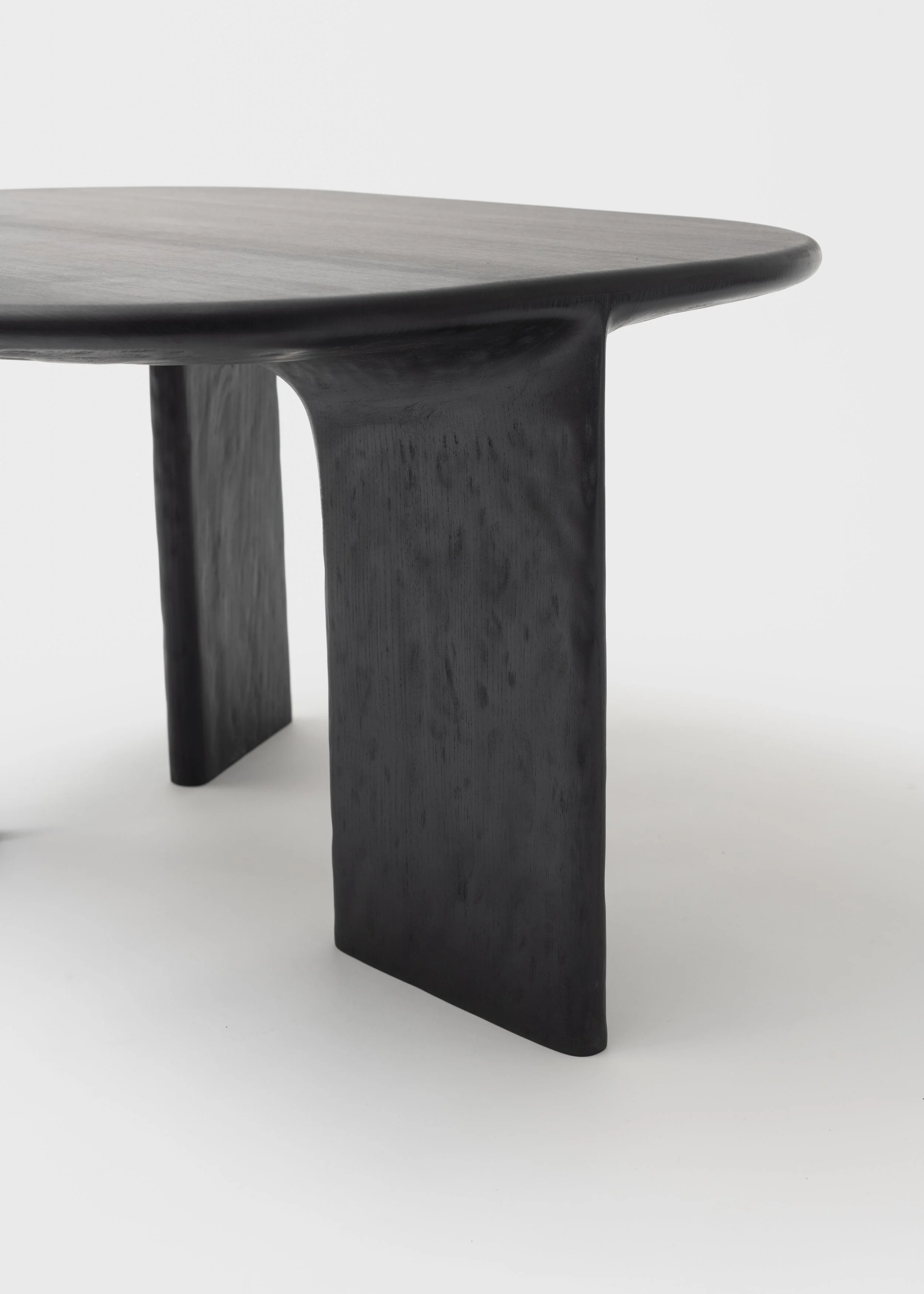 Table en bois foncé avec un plateau arrondi et des jambes larges, posé sur un fond blanc.