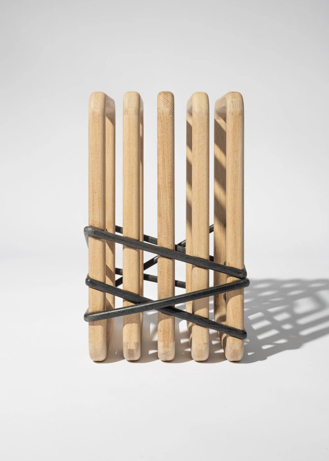 Un porte-papier toilette en bois, avec une structure en métal noir, placé sur une surface blanche. Le porte-rouleau est vide, avec un jeu d'ombres créé par la lumière.