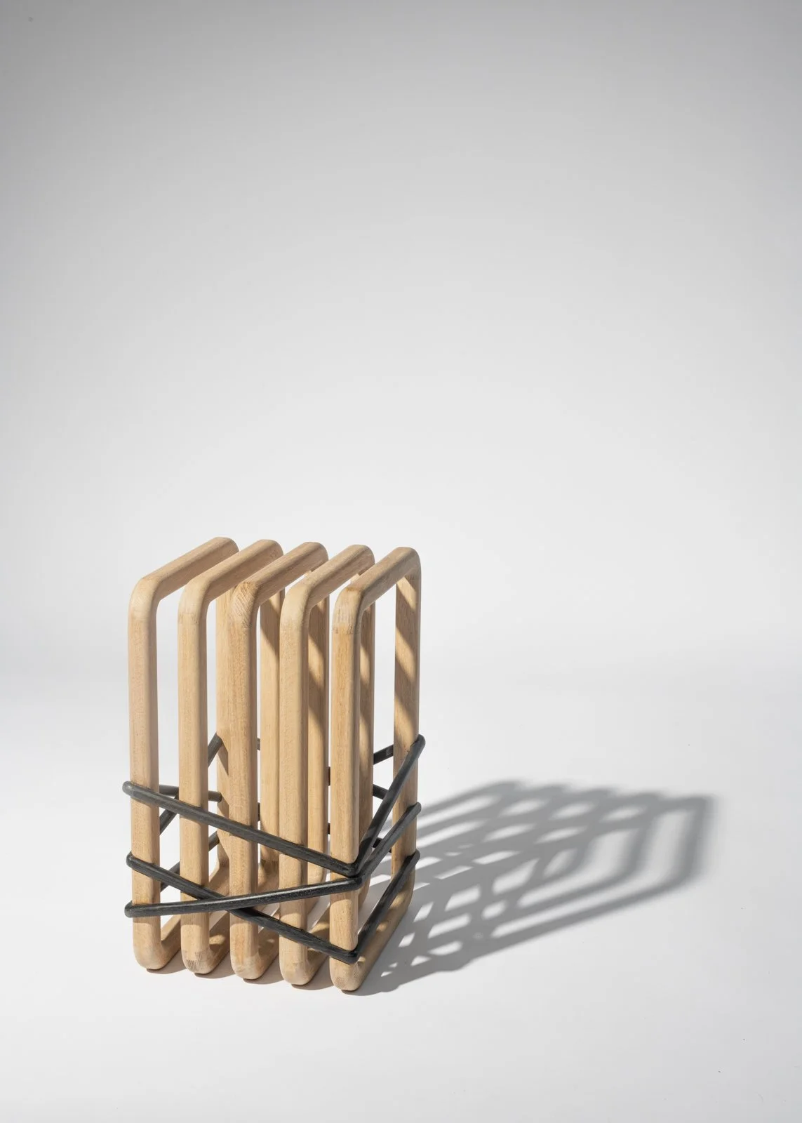 Un porte-ustensiles en bois avec des manches en forme de U, fixé avec des élastiques noirs, sur fond blanc.