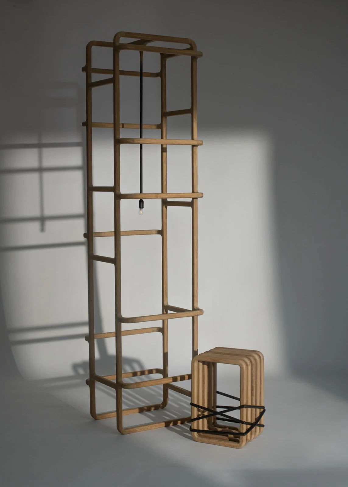 Deux étagères en bois de différentes tailles, la plus grande accrochant verticalement au mur avec une seule ampoule suspendue, et la plus petite posée au sol avec une déco en corde noire.