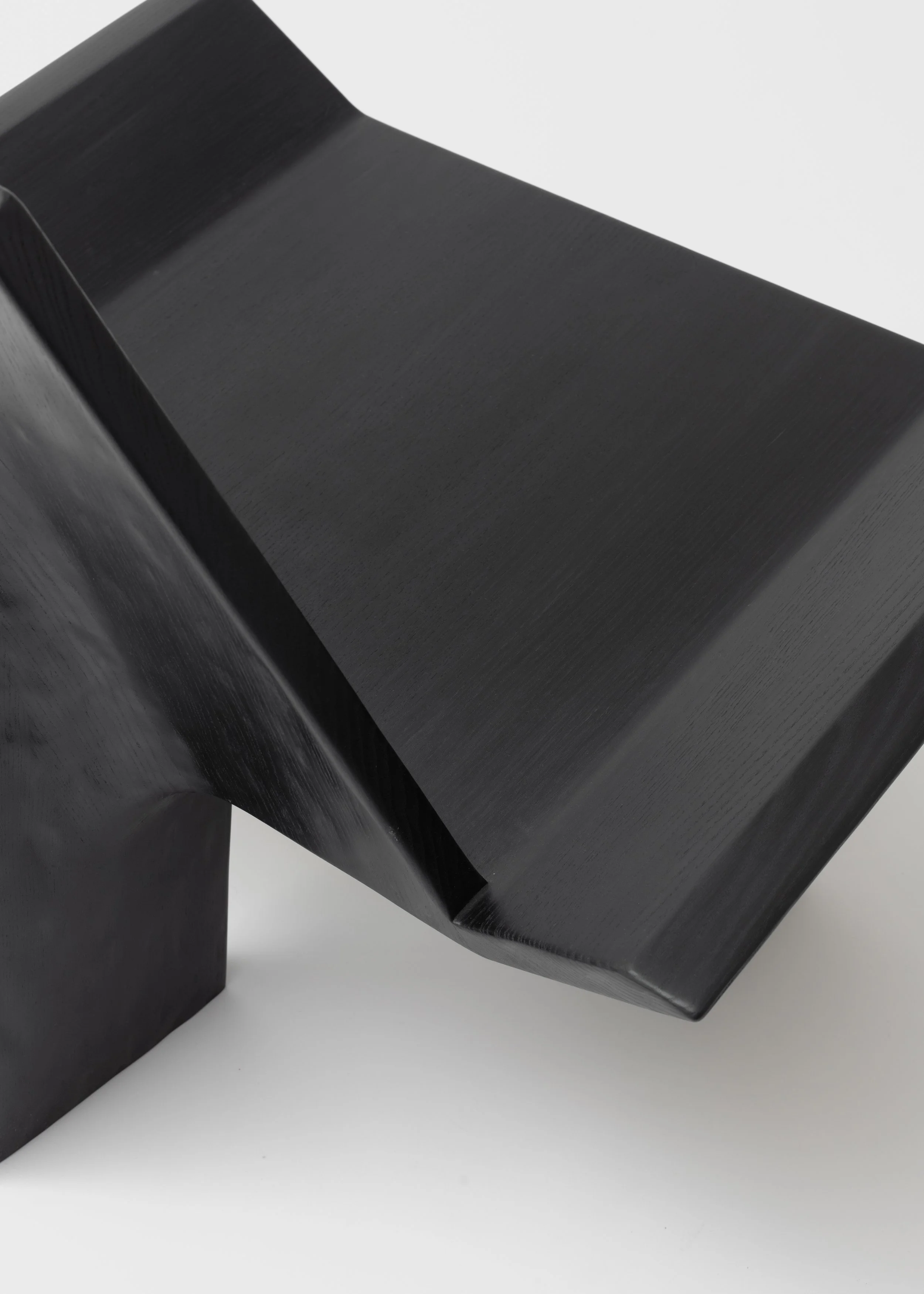 Une sculpture abstraite noire en forme rectangulaire avec des courbes élégantes, posée sur une surface blanche