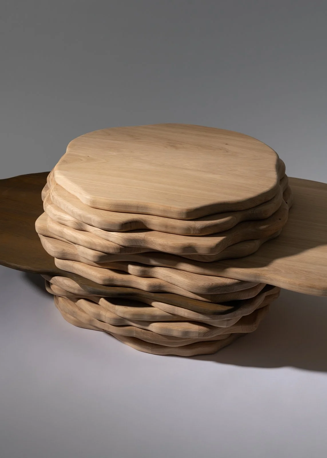 Une pile de planches en bois sculpté et waré, posée sur une surface blanche avec un fond gris.