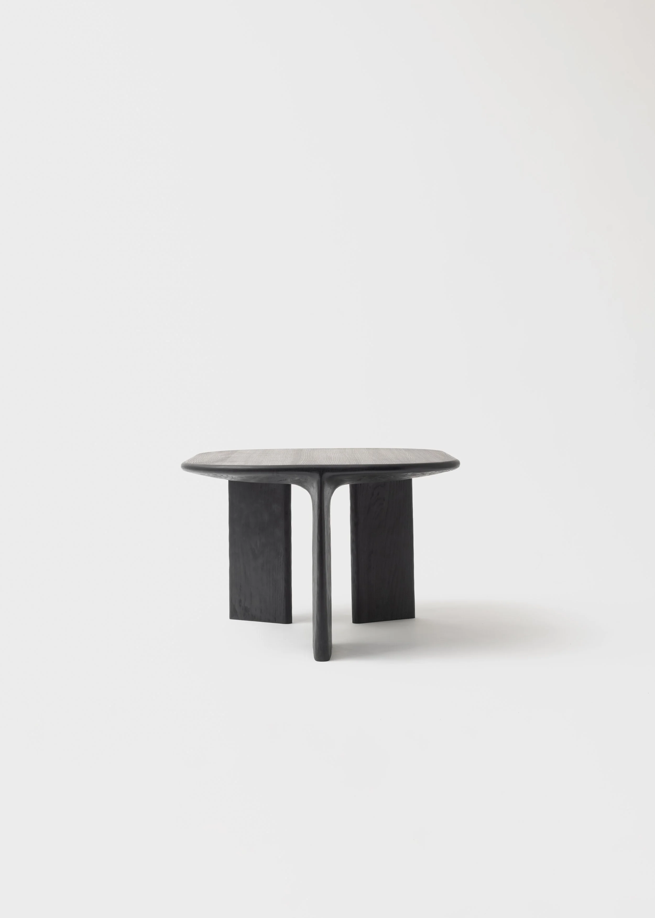 Table en bois noir avec une surface en forme d'arc et trois pieds, placé sur un fond blanc.