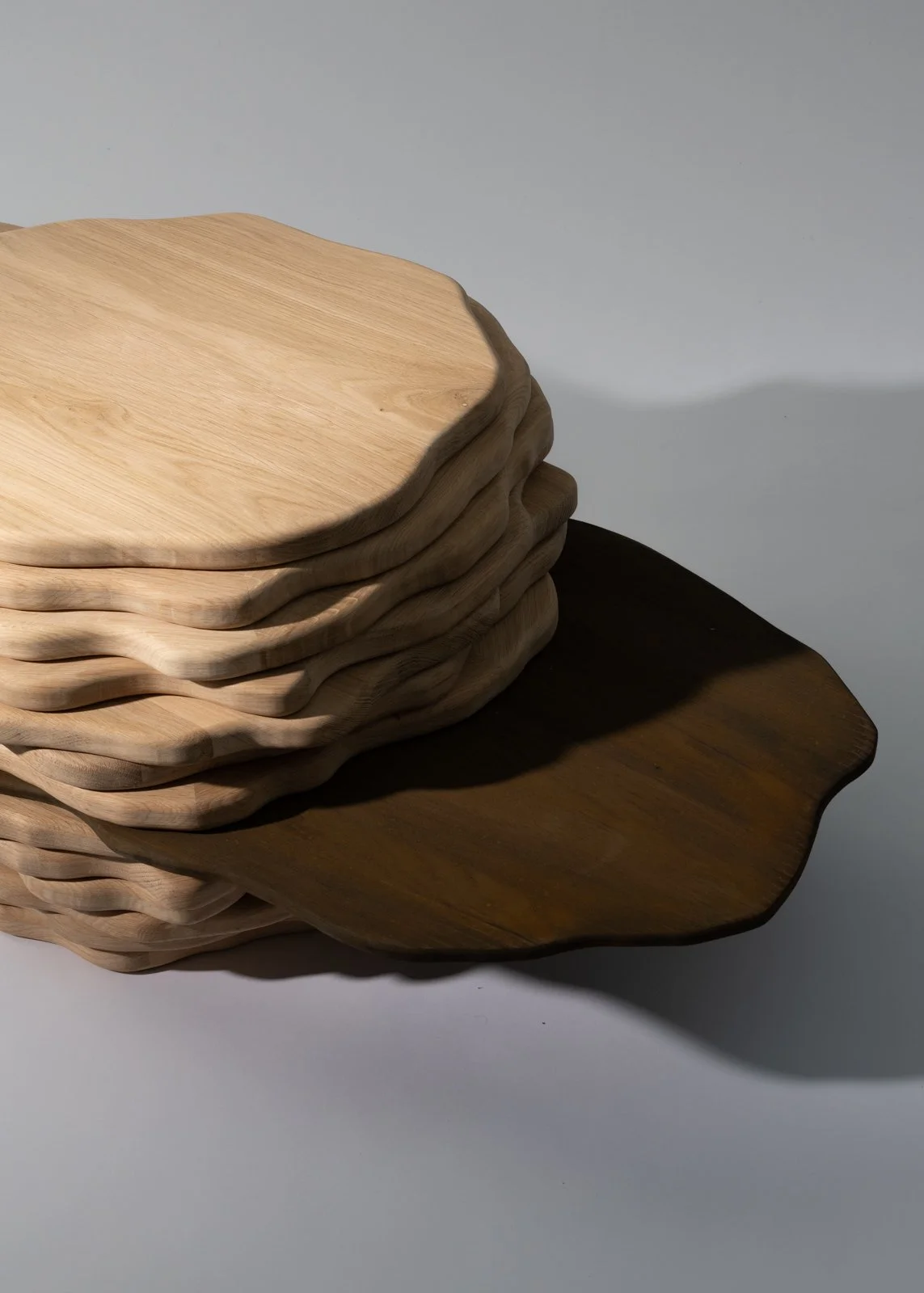 Photo d'une pile de plaques en bois de différentes teintes, avec une ombre portée sur une surface blanche.