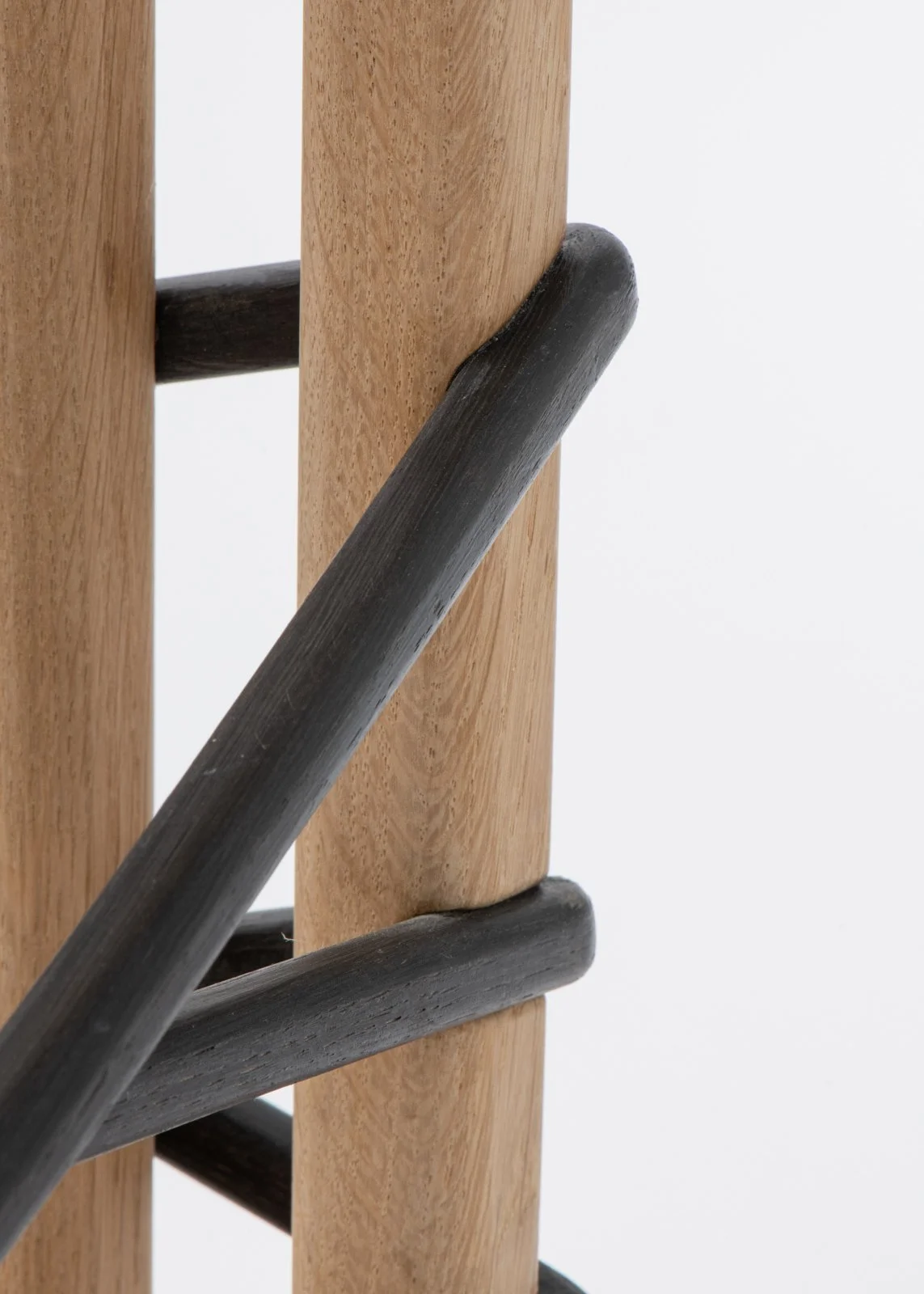 Détail d'une structure en bois avec des baguettes en bois clair et des barres en bois noir foncé, probablement un meuble ou un objet décoratif.