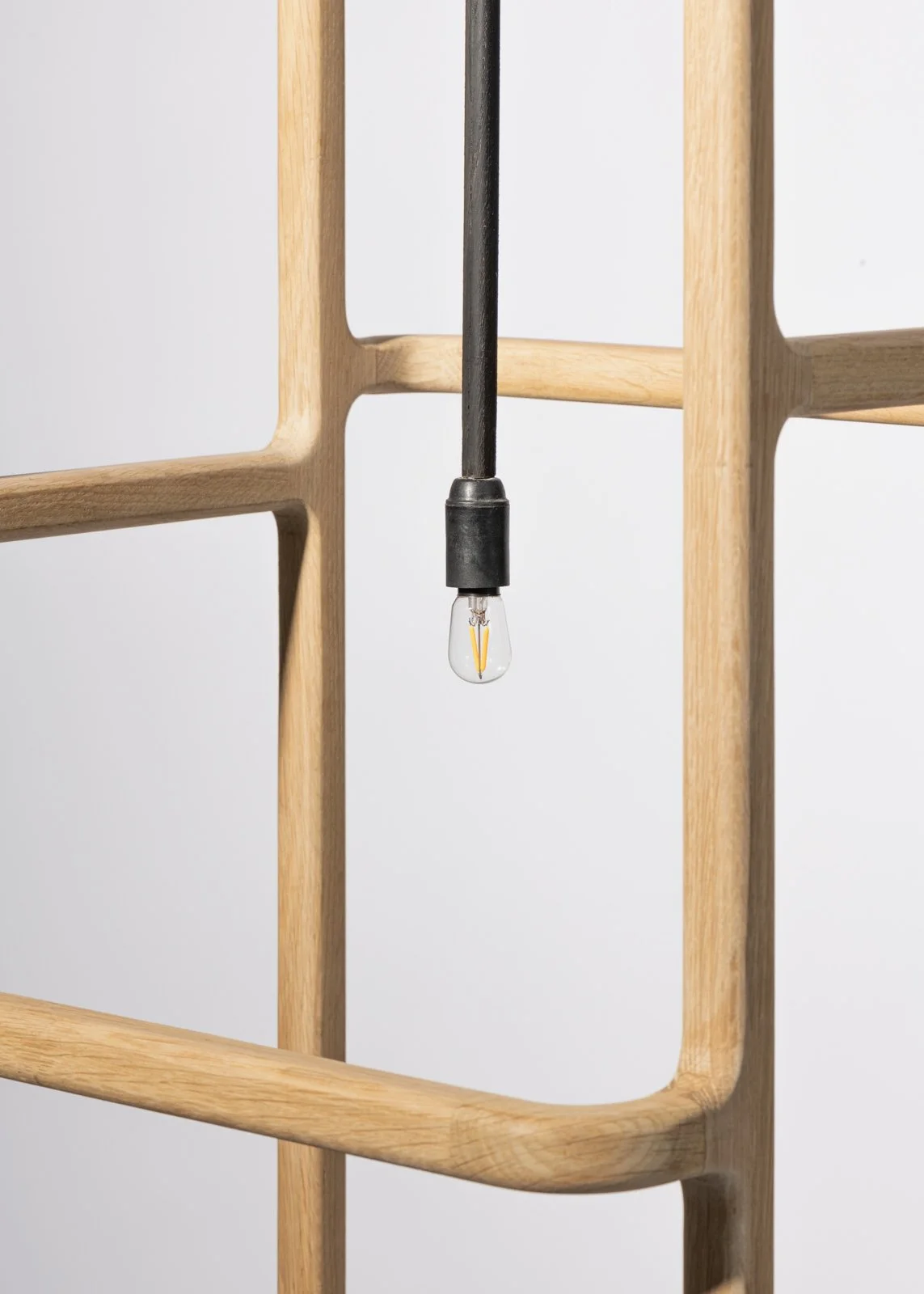 Une lampe en forme de structure en bois avec une ampoule suspendue au centre, contre un fond blanc.