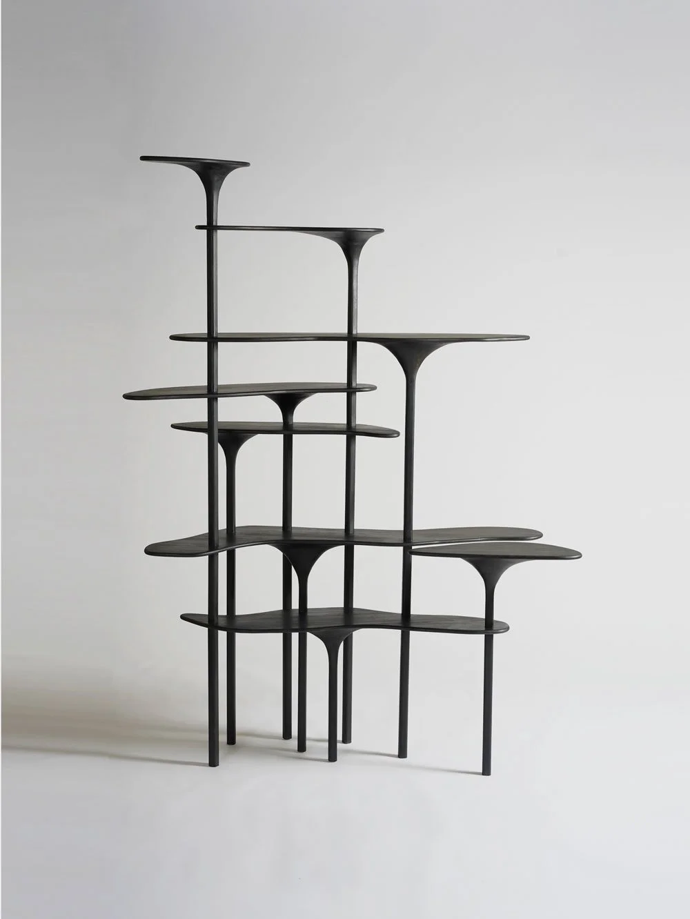 Une étagère de design moderne en bois noir avec des formes asymétriques et des plateaux suspendus, contre un fond blanc.