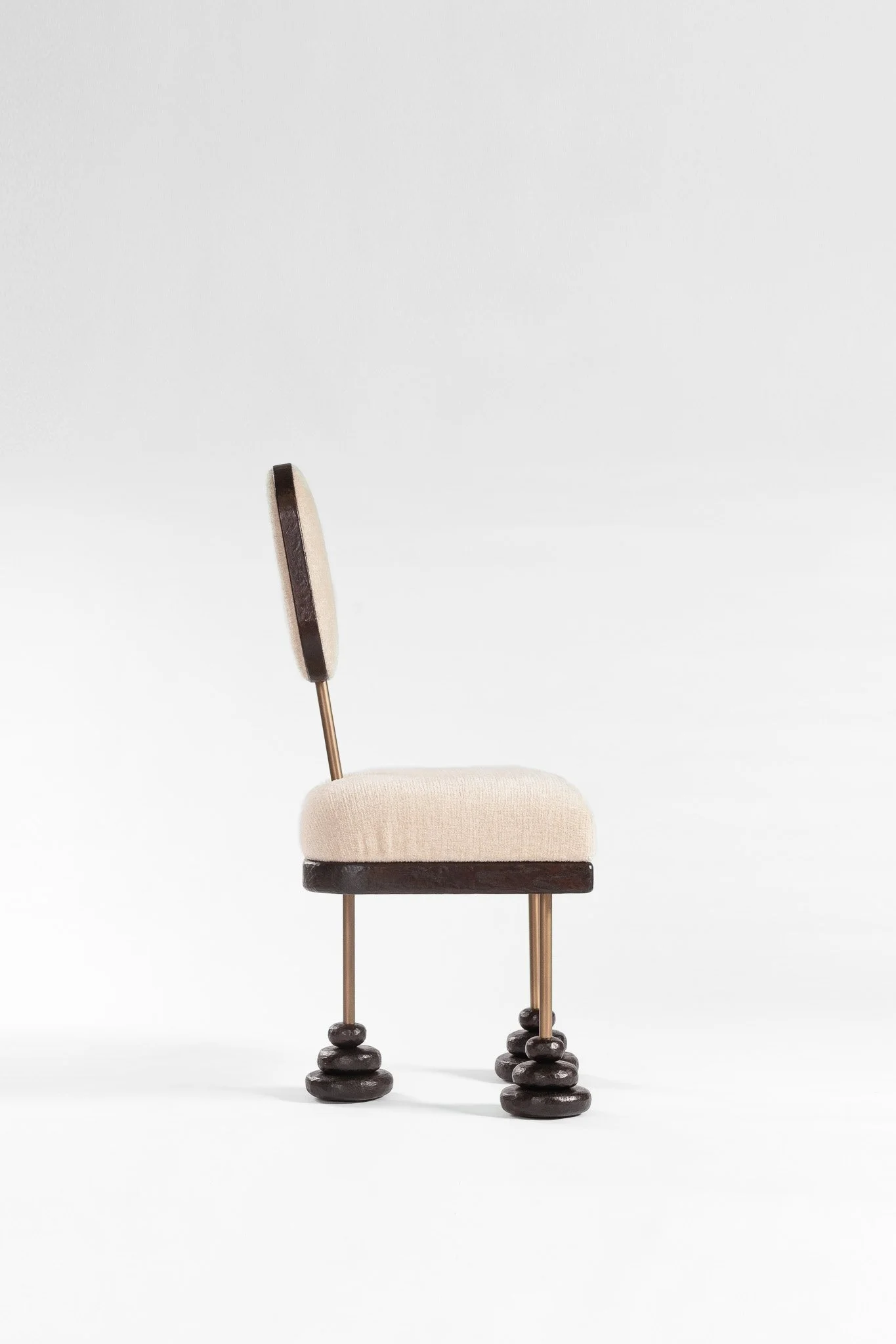 Chaise design avec des pieds en forme de petits tas en bois foncé et une assise rembourrée en tissu clair, vue de côté sur fond blanc.