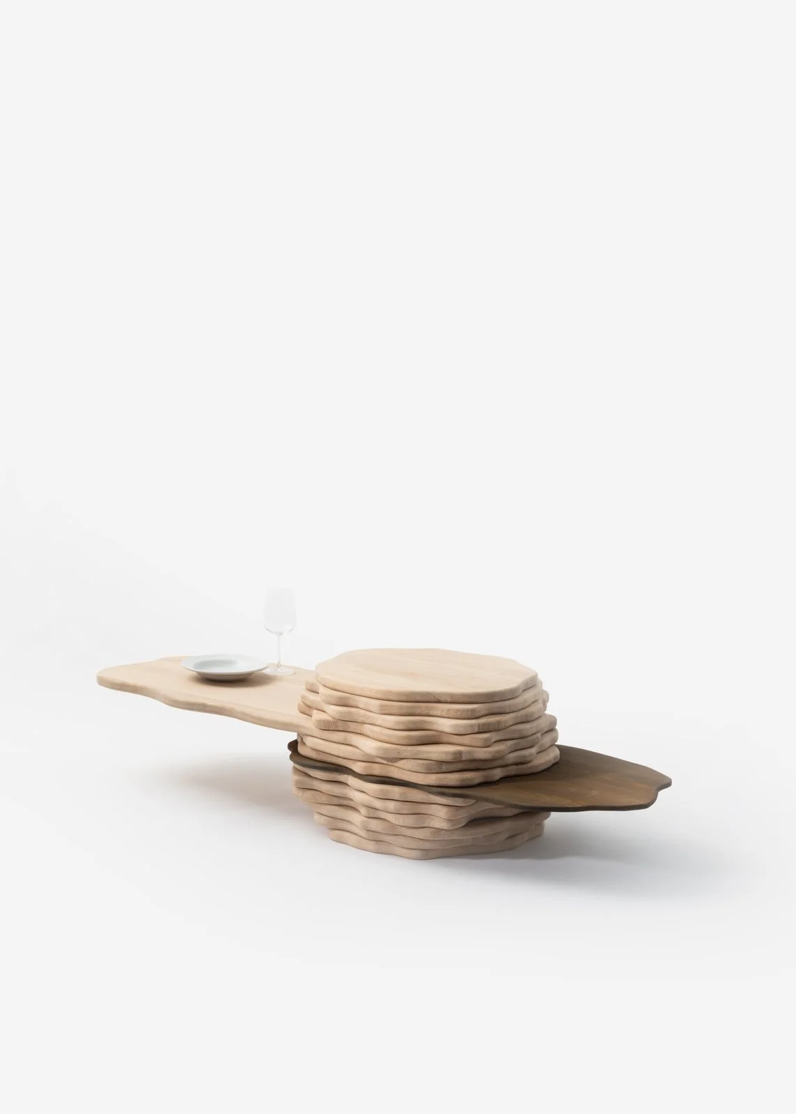 Table en bois avec une pile d'assiettes en bois, une table en bois clair, un verre à vin vide et une petite assiette blanche.