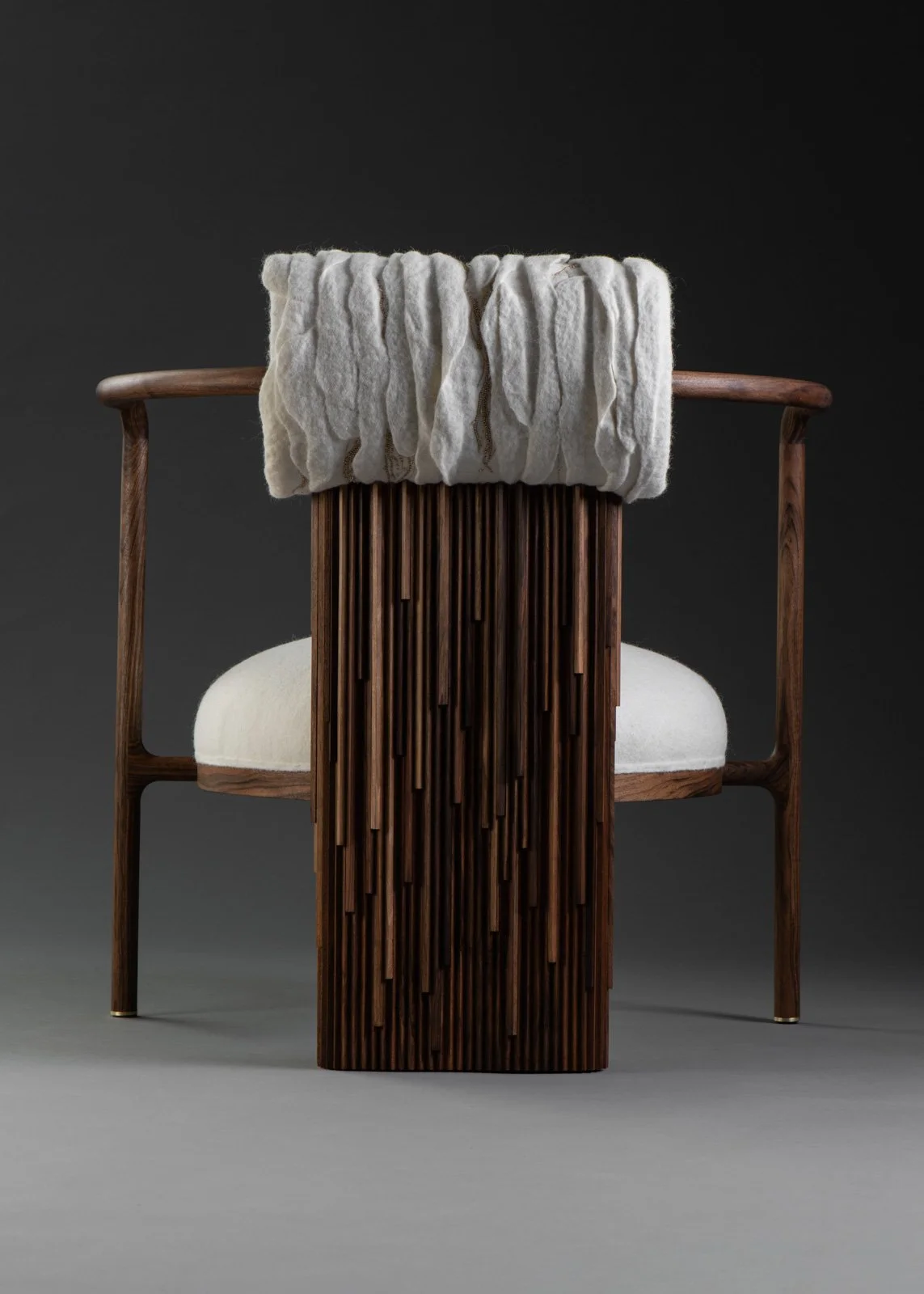 Chaise en bois avec un coussin blanc et une couverture blanche en laine, sur un fond gris foncé.