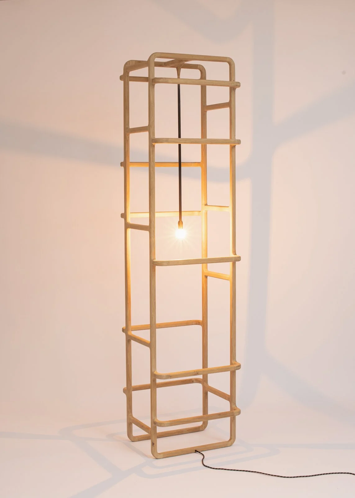 Lampe de salon en forme de cadre en bois avec une ampoule suspendue au centre, projetant des ombres sur le mur blanc.