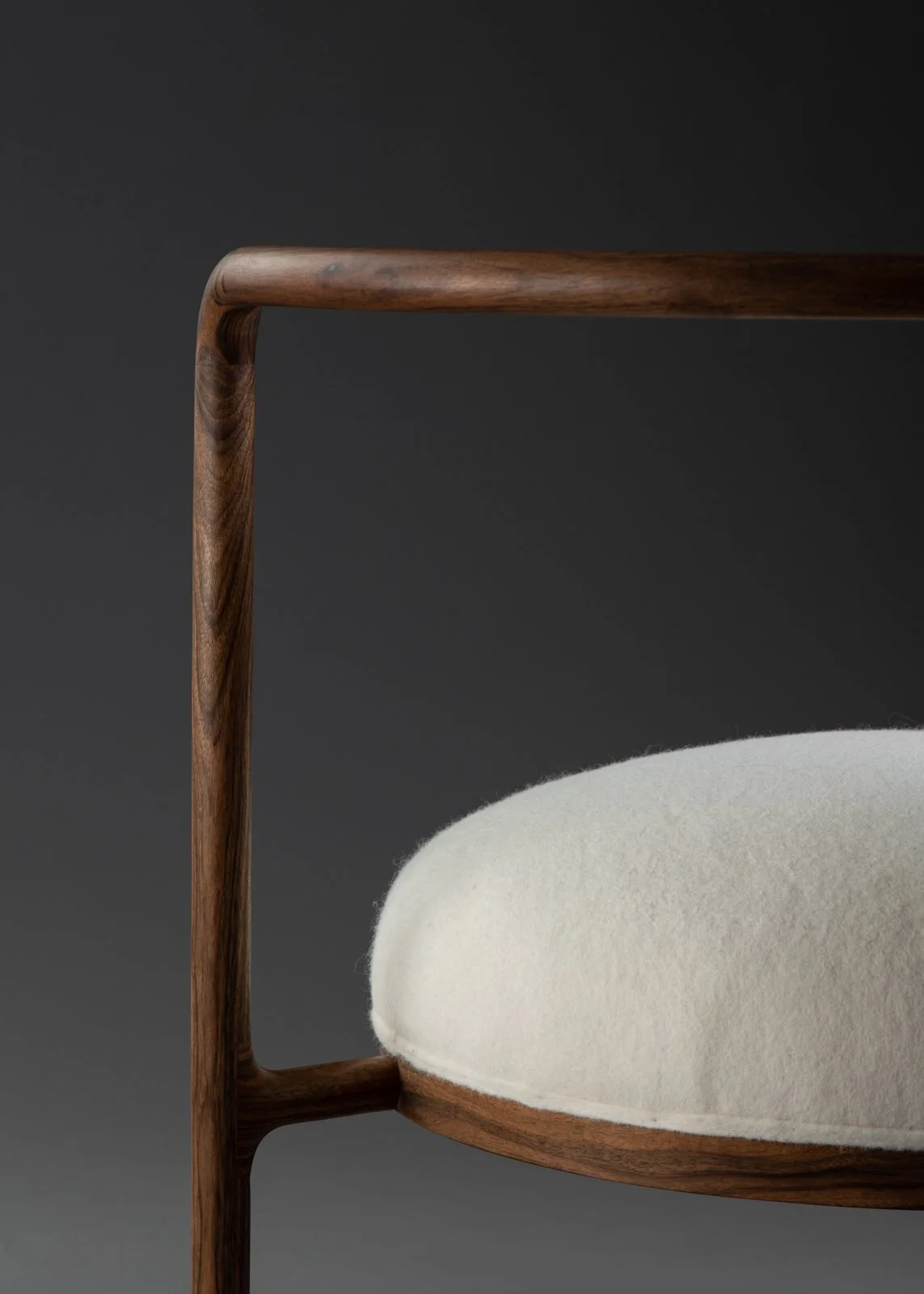 Une chaise en bois avec un coussin blanc cassé contre un fond gris foncé.