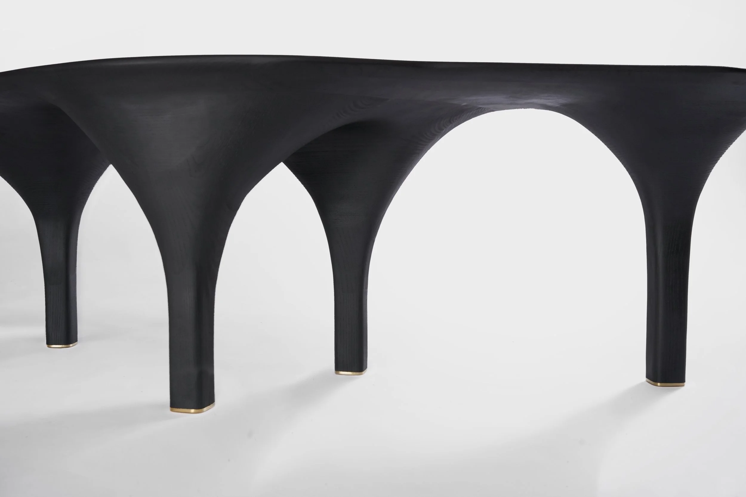 Table noire avec des jambes en forme d'arcs, posé sur un fond blanc