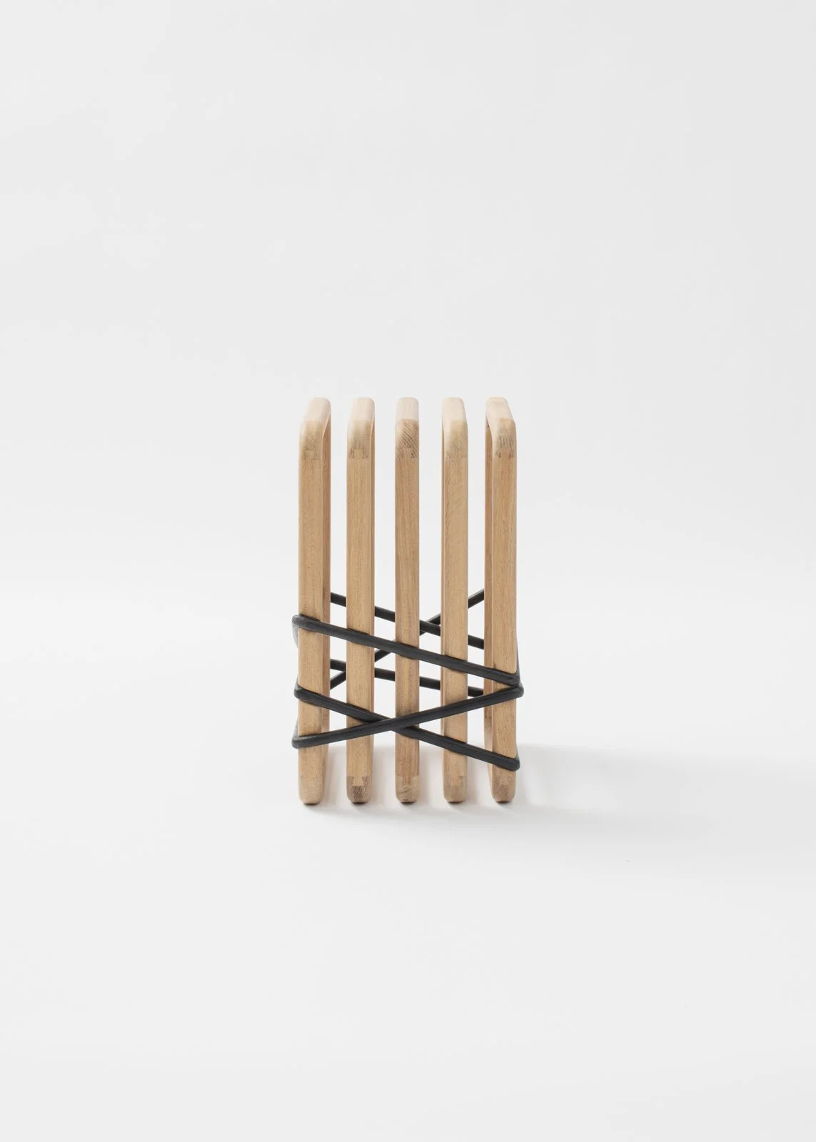 Un tabouret en chêne massif fait de six baguettes en bois fixées par un cordon noir.