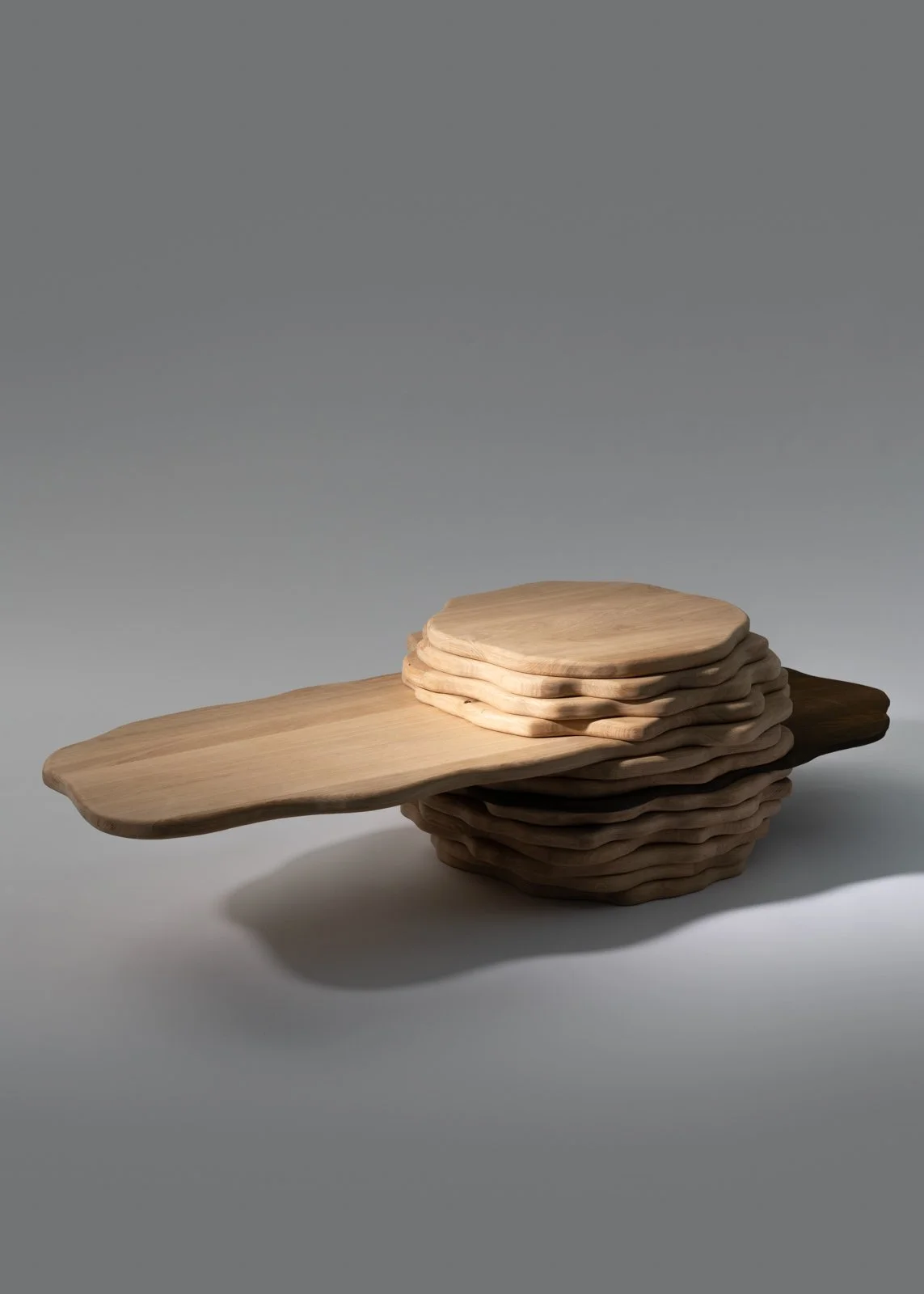 Une pile de planches en bois naturelles, avec une planche plate qui s'étend à partir de la pile, sur un fond gris clair.
