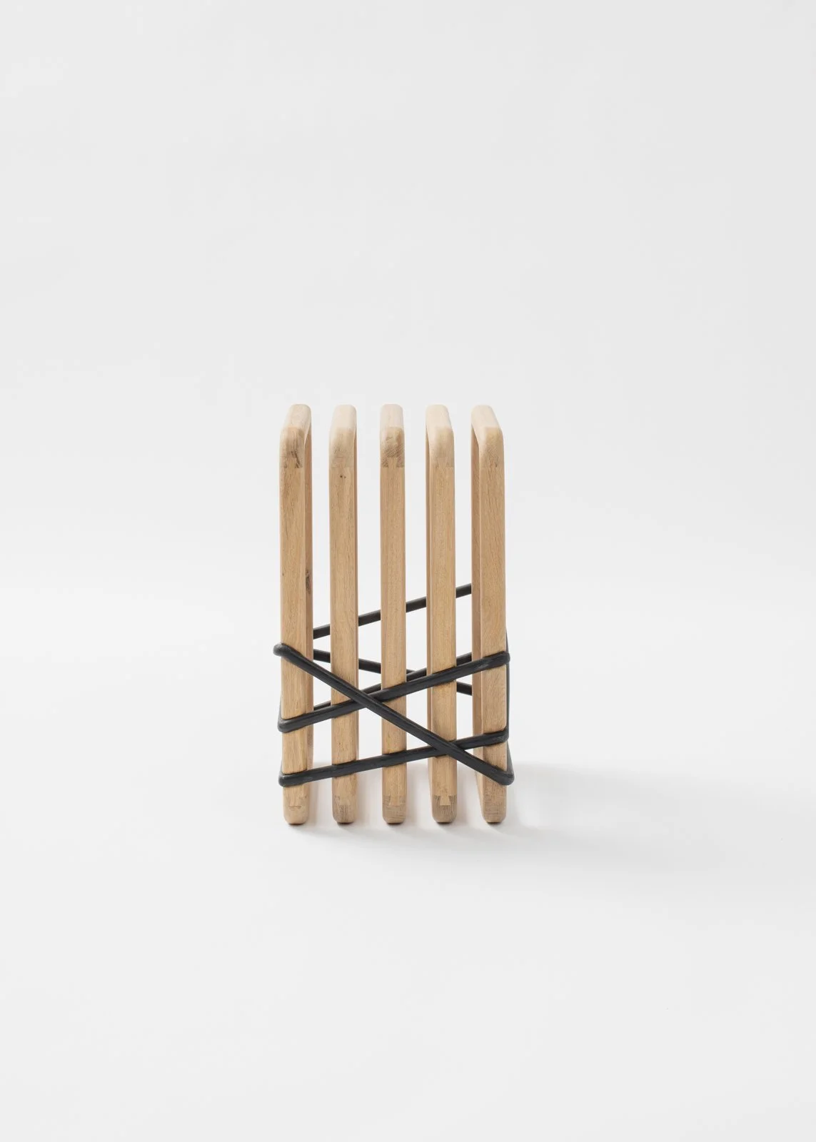 Un tabouret en bois avec des bandes de bois noires enroulées autour, posé sur un fond blanc.