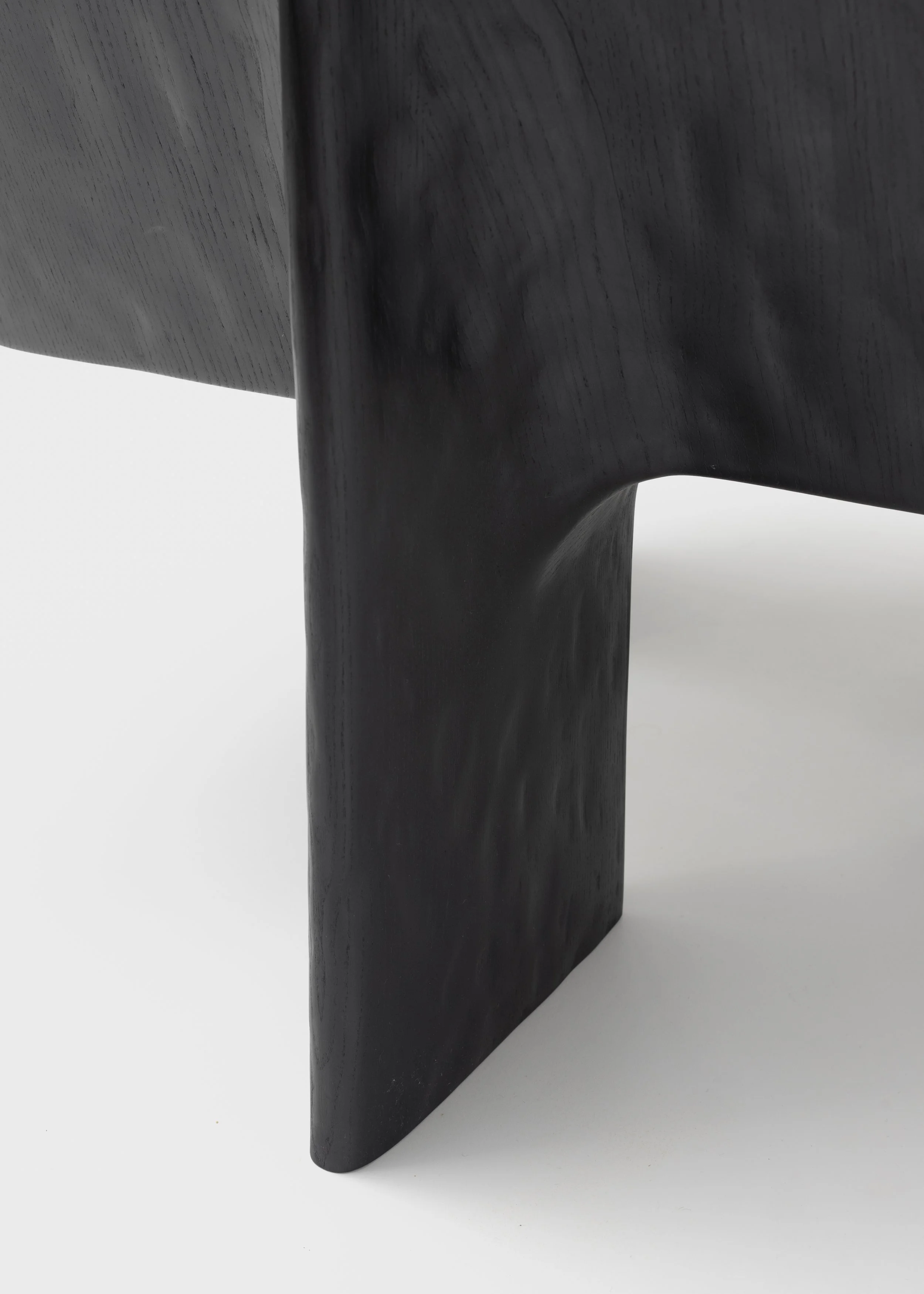 Pied en bois noir d'un meuble ou d'une sculpture, avec une surface lisse et un fini mat, posé sur un sol blanc.