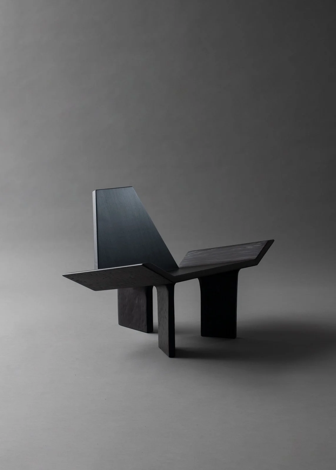 Un meuble moderne en bois noir, ressemblant à une chaise ou à un banc, placé sur un fond gris.