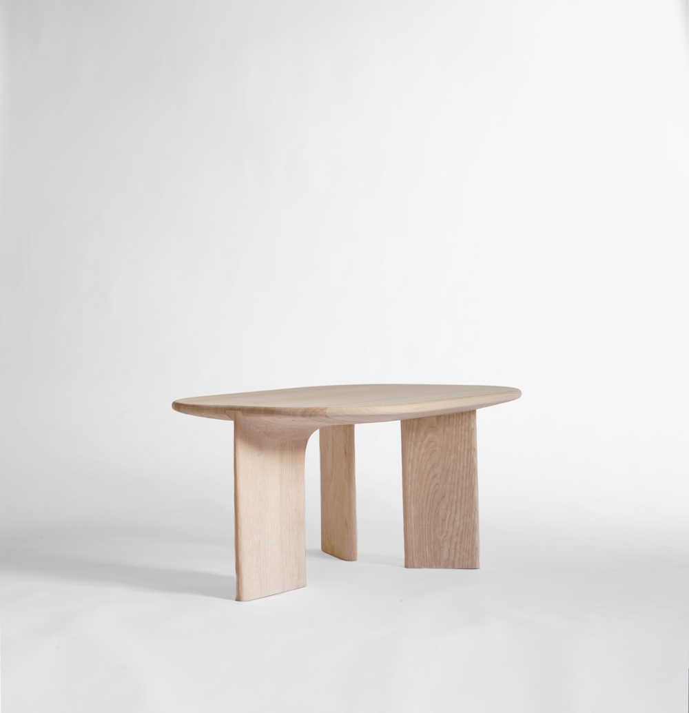 Table en bois clair avec un plateau ovale et deux jambes épaisses, placé sur un fond blanc