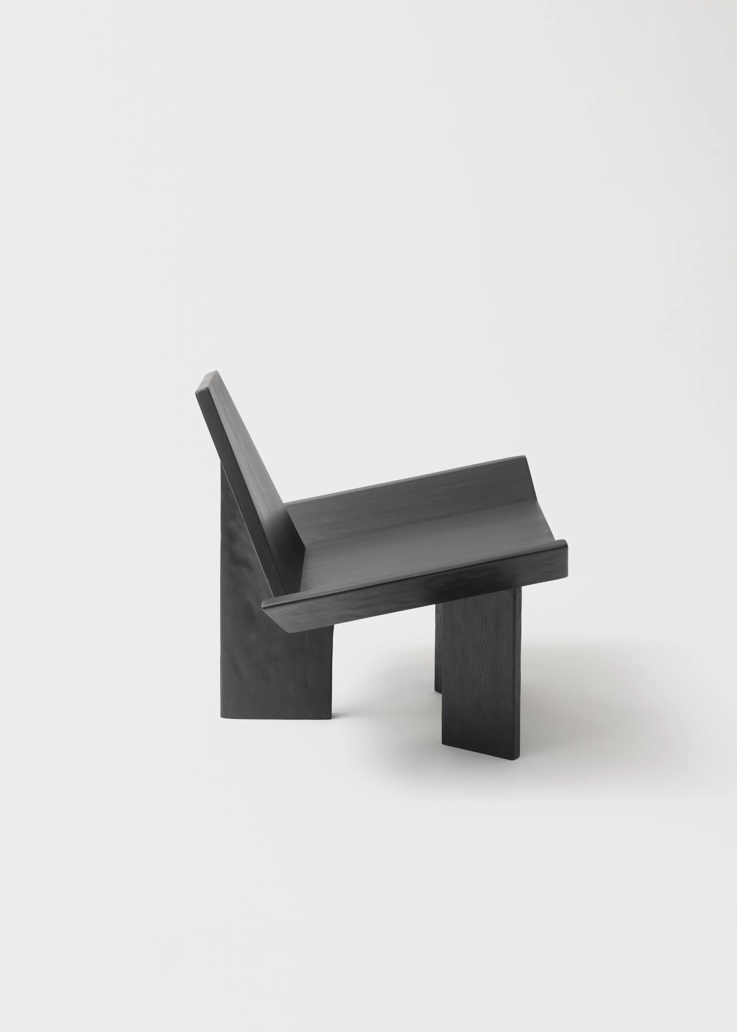 Une petite chaise noire en bois avec un design minimaliste, placée sur un fond blanc.