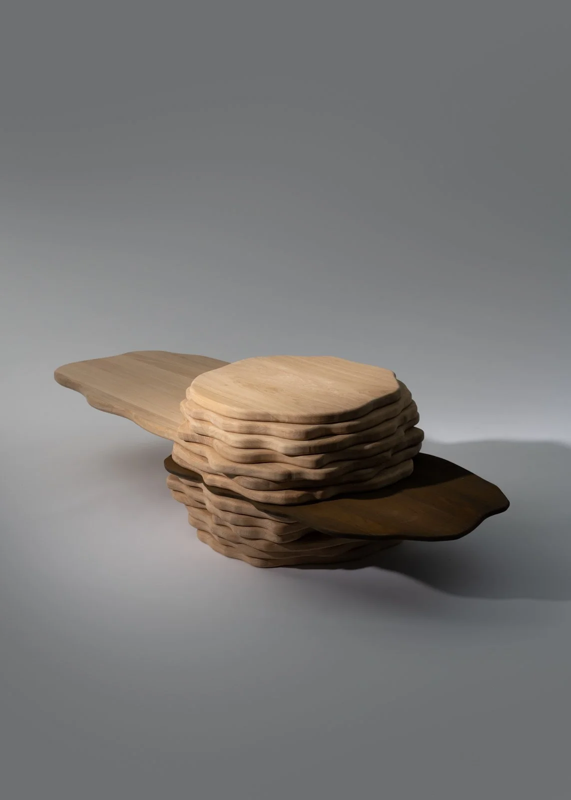 Empilement de plaques en bois de différentes teintes, disposées de manière artistique sur une surface neutre.