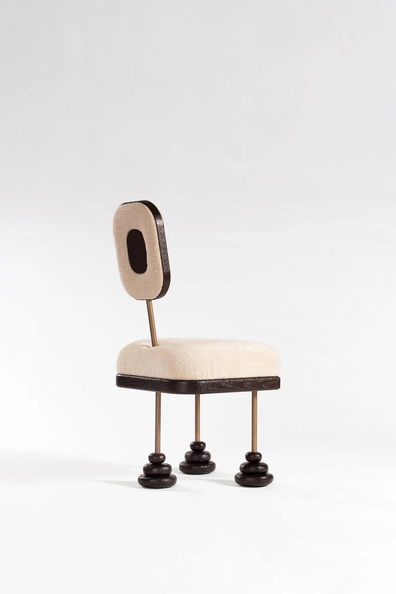 Chaise moderne avec un design artistique, assise rembourrée beige, dossier ovale en bois noir, pieds en métal avec décorations en bois, placé sur un fond blanc clair.