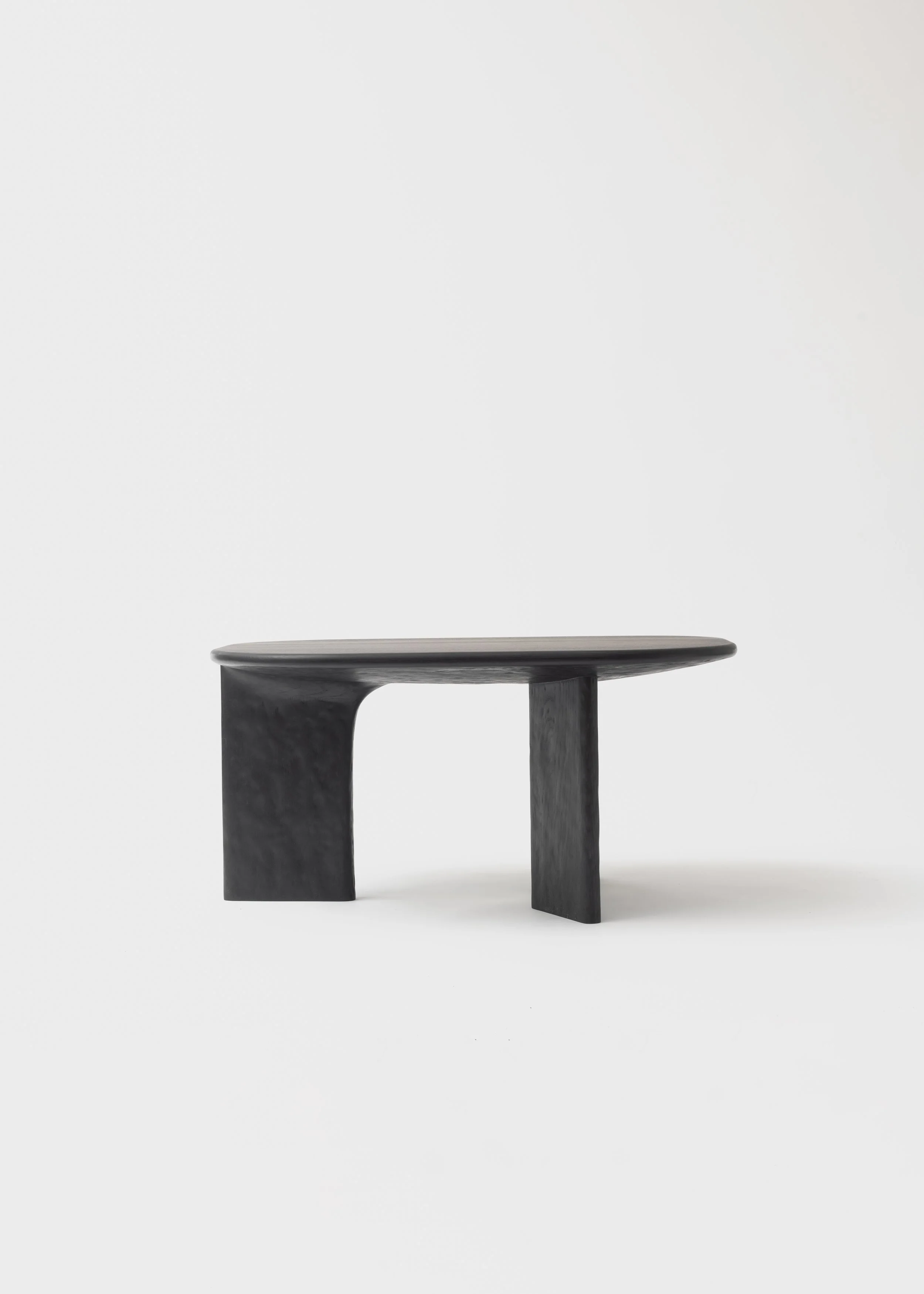 Table basse design en bois noir avec piètement artistiquement incurvé, placé contre un fond blanc.
