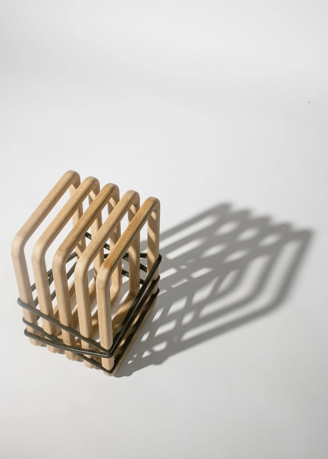 Un porte-couverts en métal noir contenant plusieurs cuillères en bois, projetant une ombre sur une surface blanche.