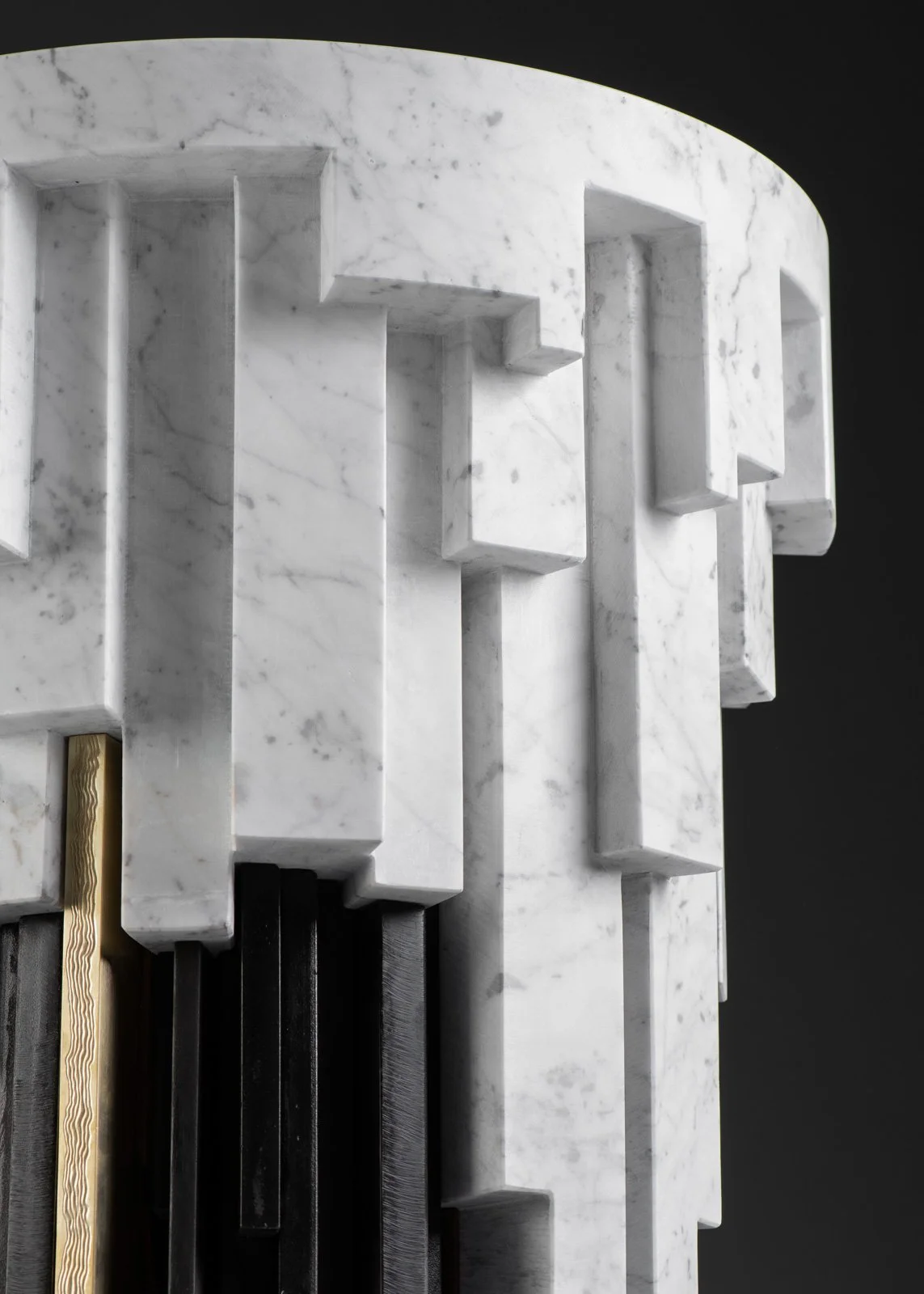 Structure moderne en marbre blanc avec des formes géométriques en relief, contre un fond noir.