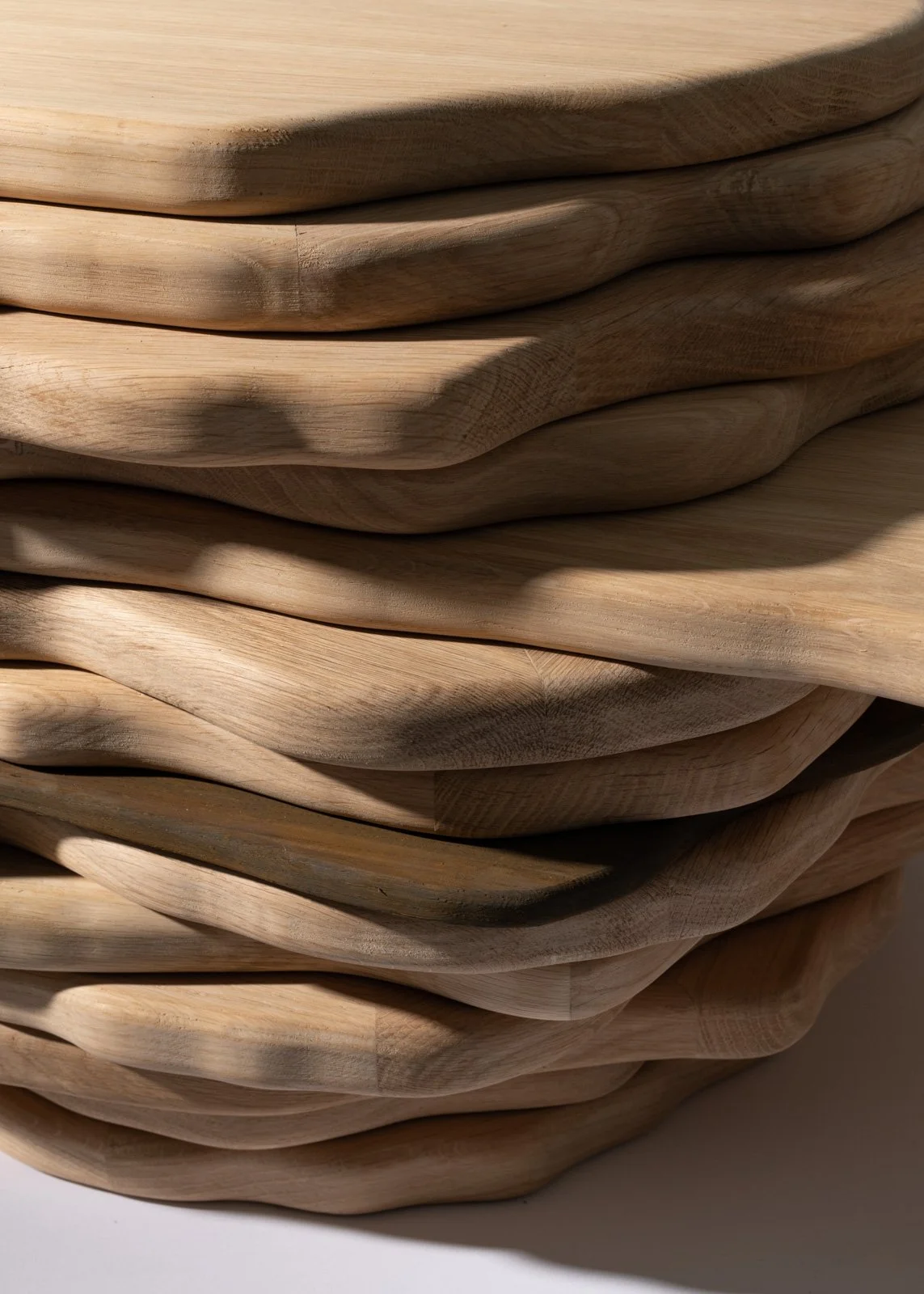 Une pile de planches en bois avec des formes organiques, éclairée par la lumière, créant des ombres.