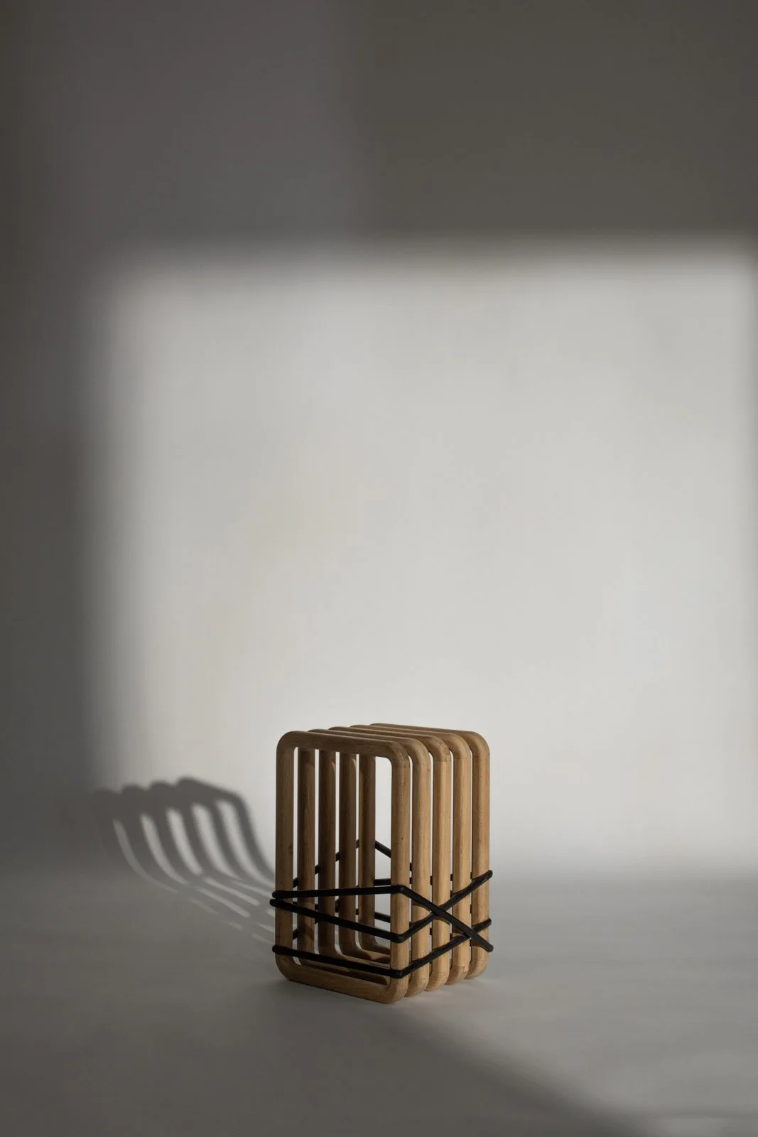 Un ensemble d'objets en bois en forme de rectangles empilés, fixé ensemble avec une bande noire, placé sur une surface blanche, avec une ombre prolongée sur le mur en arrière-plan.