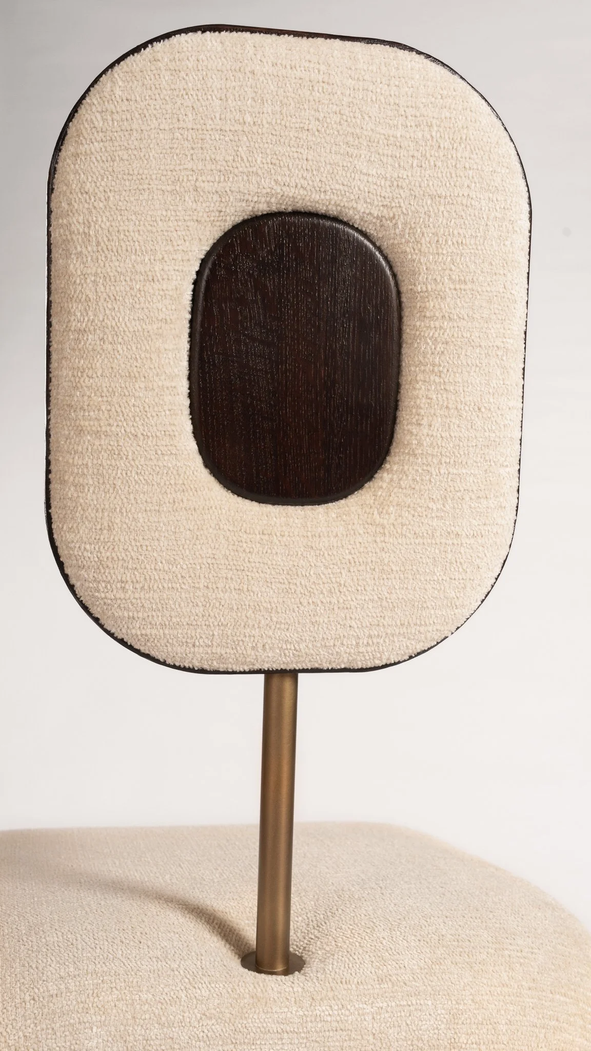 Une chaise design avec un dossier ovale couverte de tissu beige, un support en métal et une assise également en tissu beige.