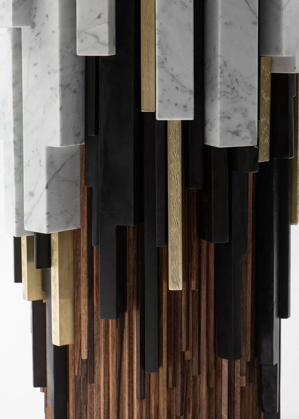 Une sculpture murale composée de différentes formes de pierres, bois et matériaux métalliques, disposés verticalement dans un design moderne.