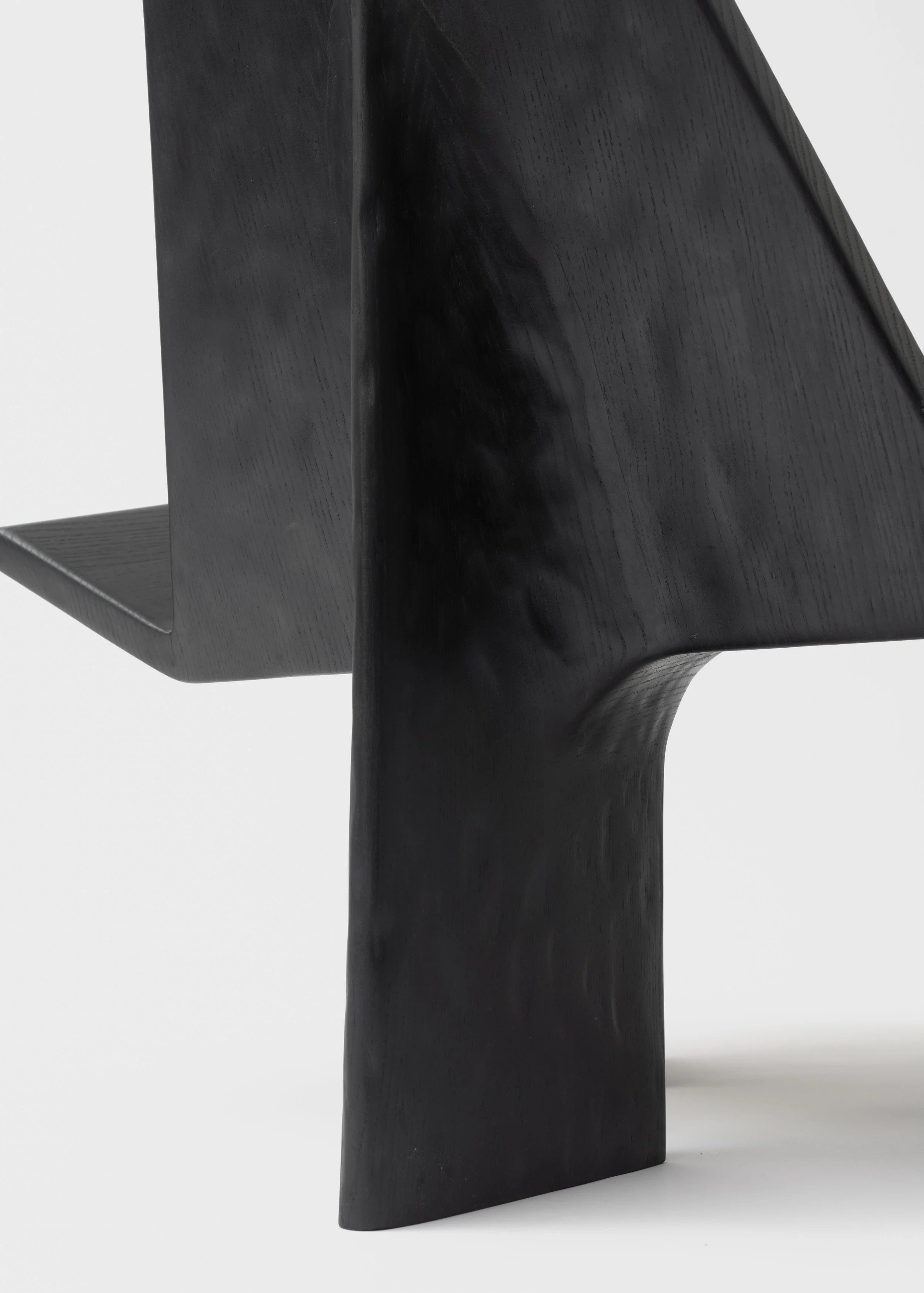 une sculpture noire en bois avec une forme contemporaine, vue de côté contre un fond blanc.