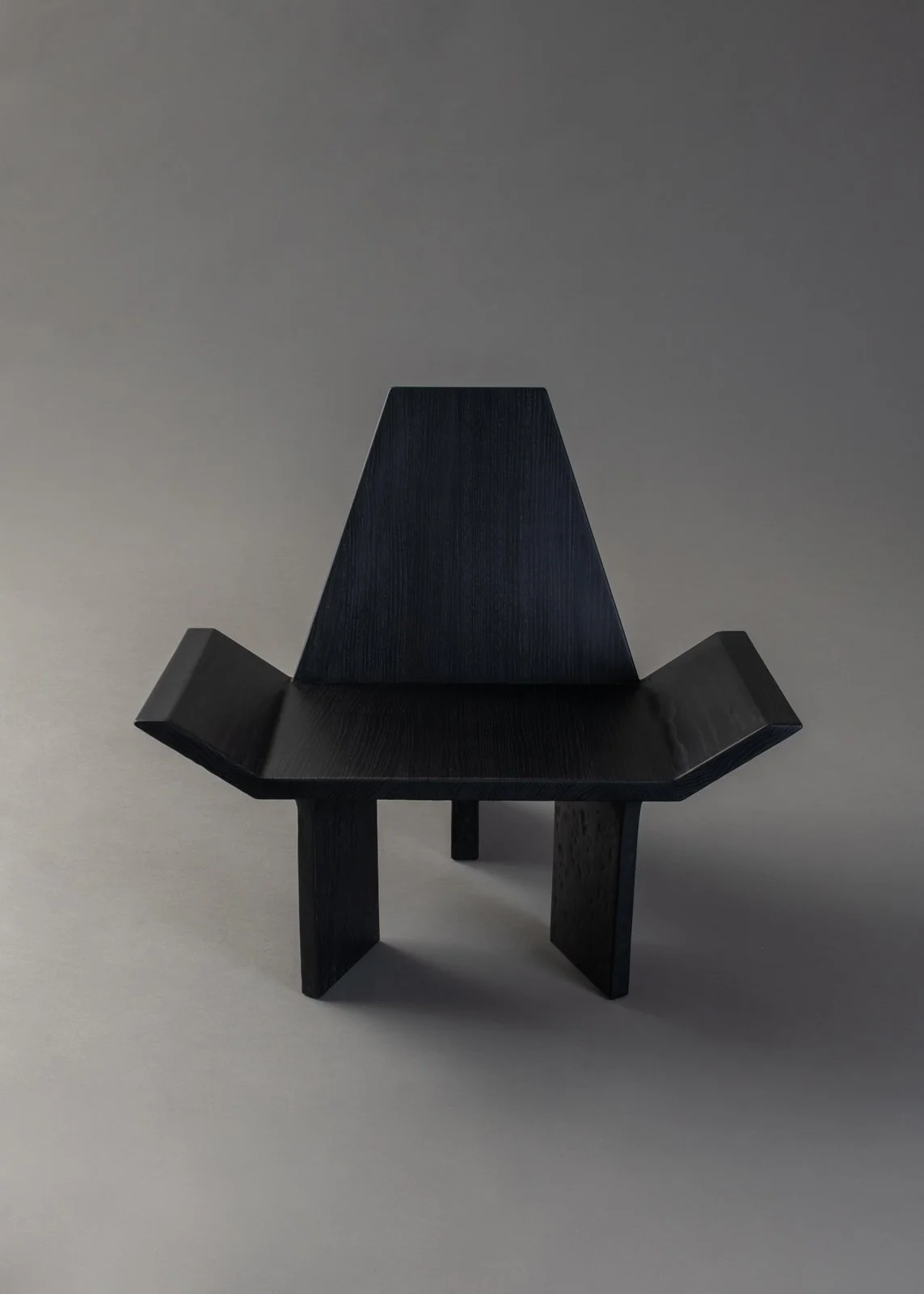 Une petite chaise en bois noire, avec un design moderne et minimaliste, placée sur un fond gris clair.