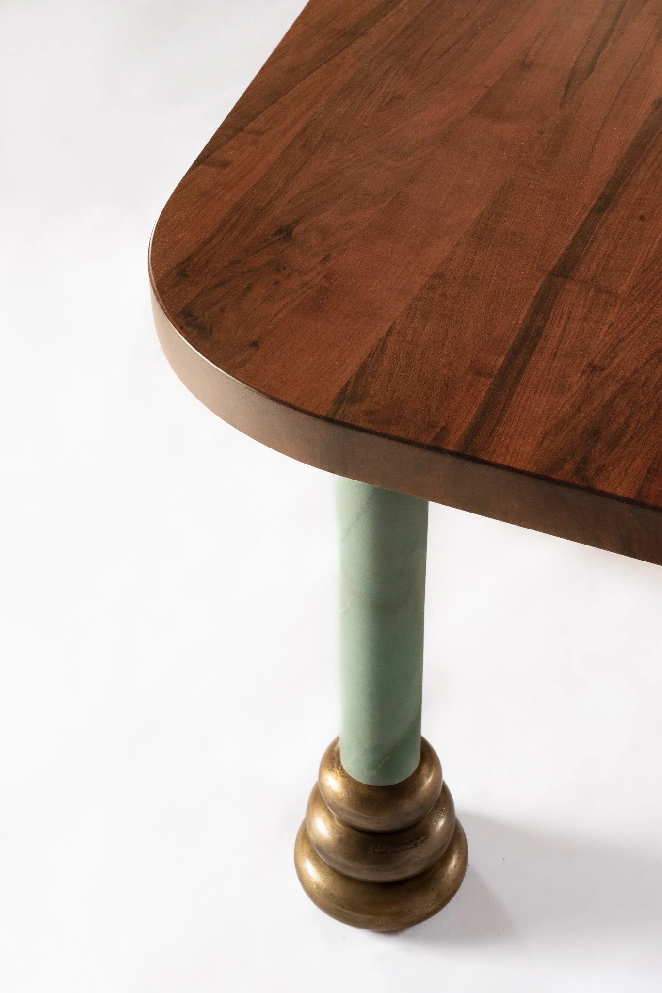 Détail d'une table en bois avec un pied en forme de boule en métal doré et une jambe en bois peint en vert.