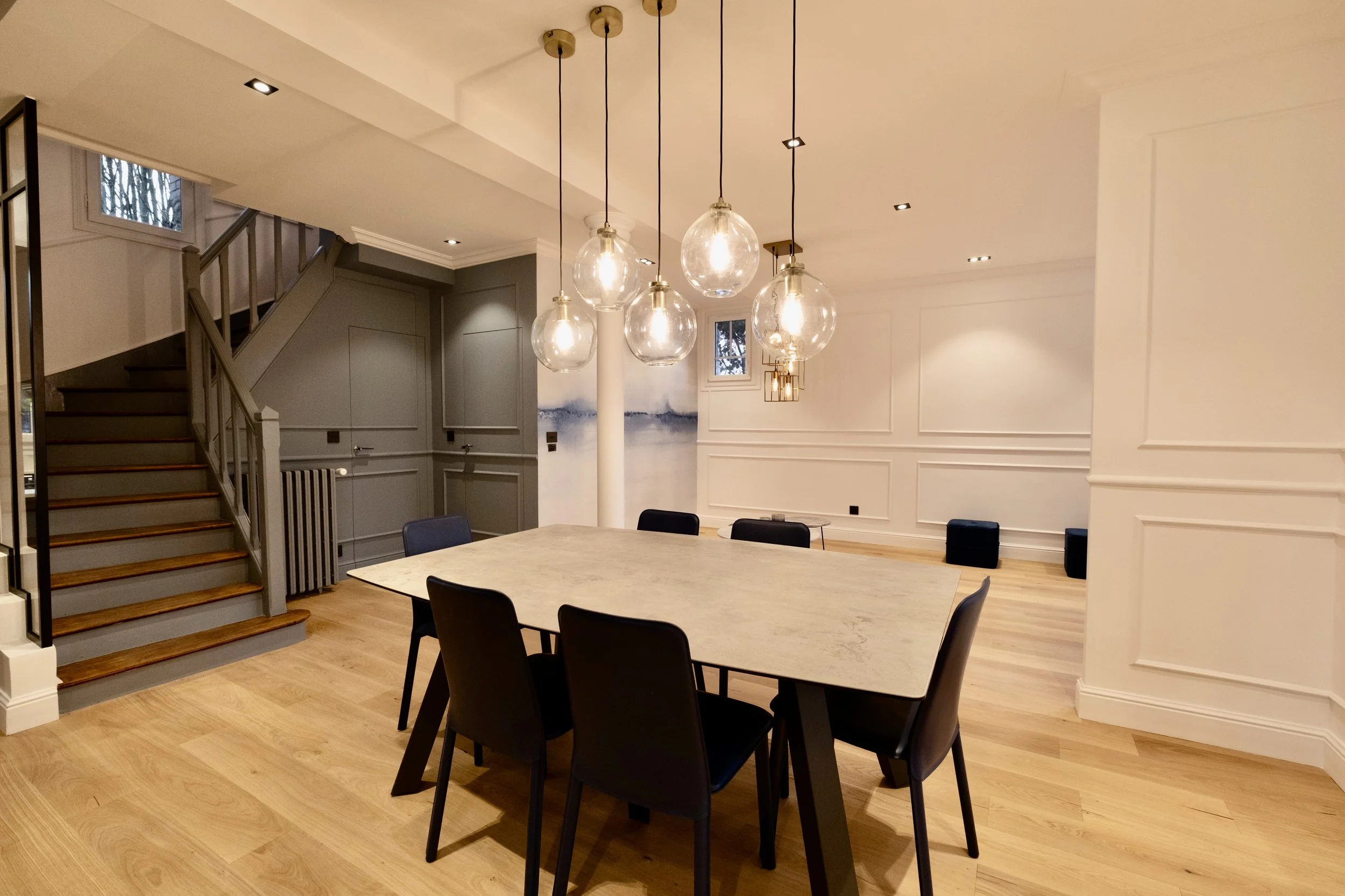 Salle à manger rénovée avec suspensions en verre, moulures et escalier en bois