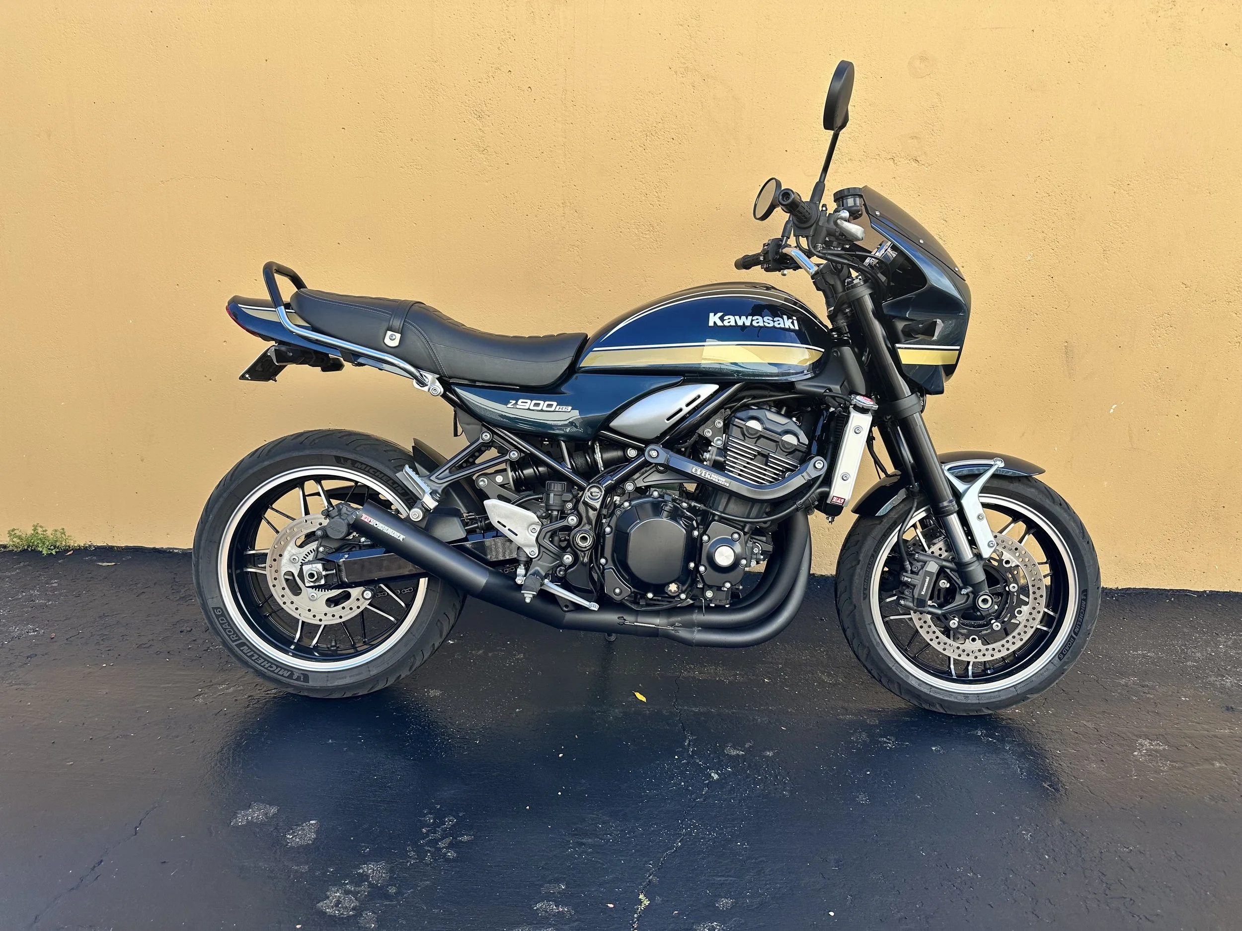 A black and blue Kawasaki Z900 motorcycle parked on asphalt in front of a beige wall.